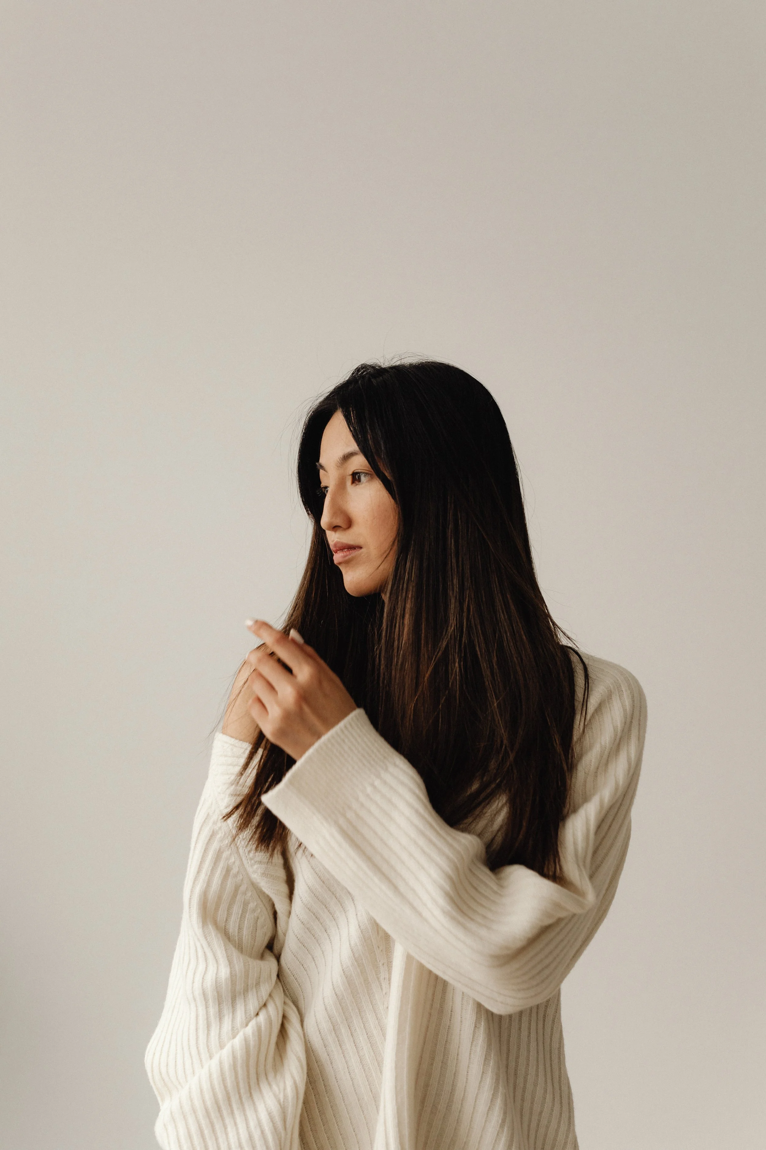 A woman with long dark hair wearing a cream-colored, ribbed blazer standing against a plain, light background.