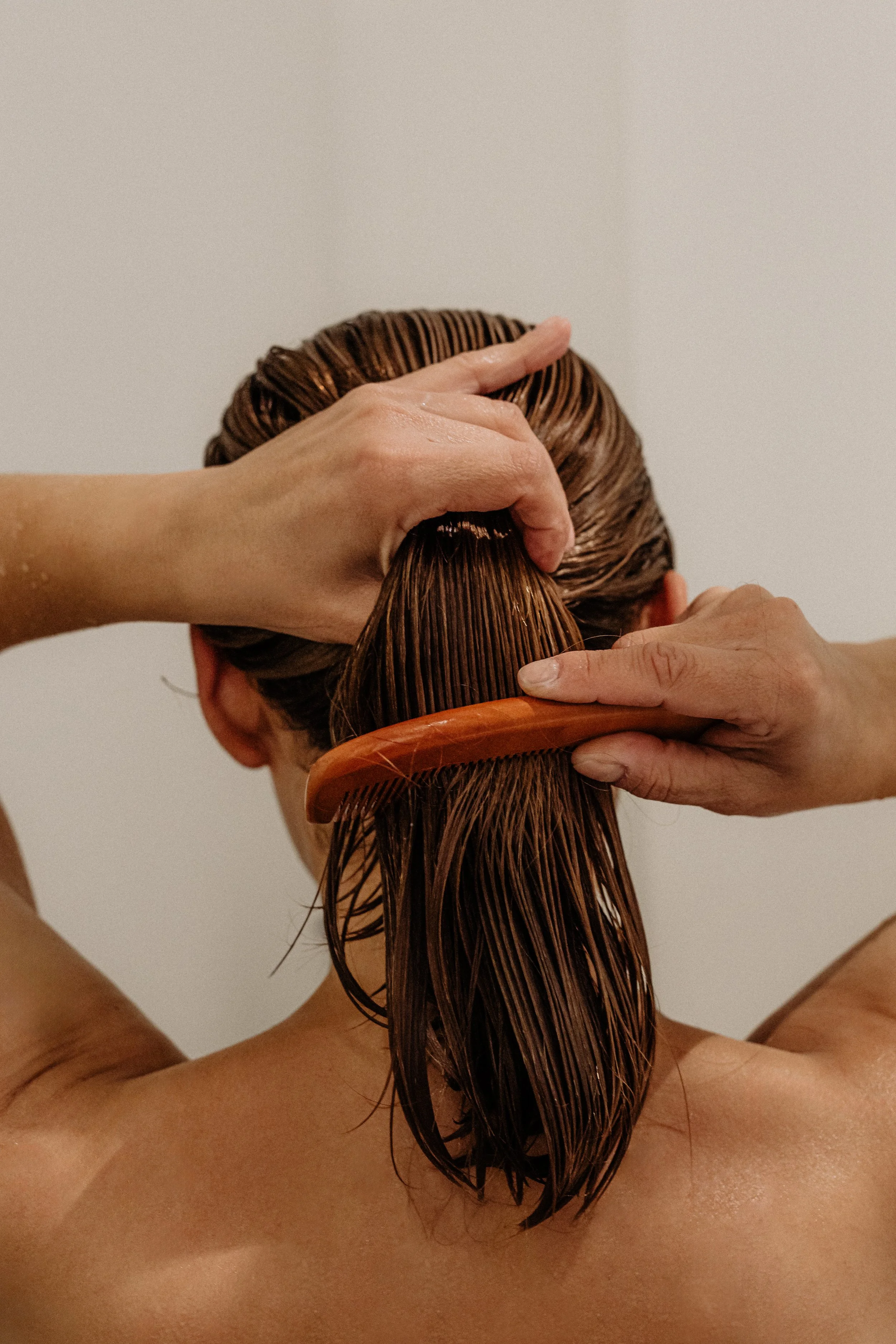 Person getting a hair wash, with water and hair conditioner being applied with a wooden brush and hands.