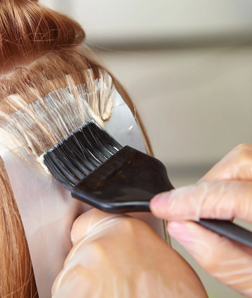 A person applying hair dye with a brush to long, red hair.