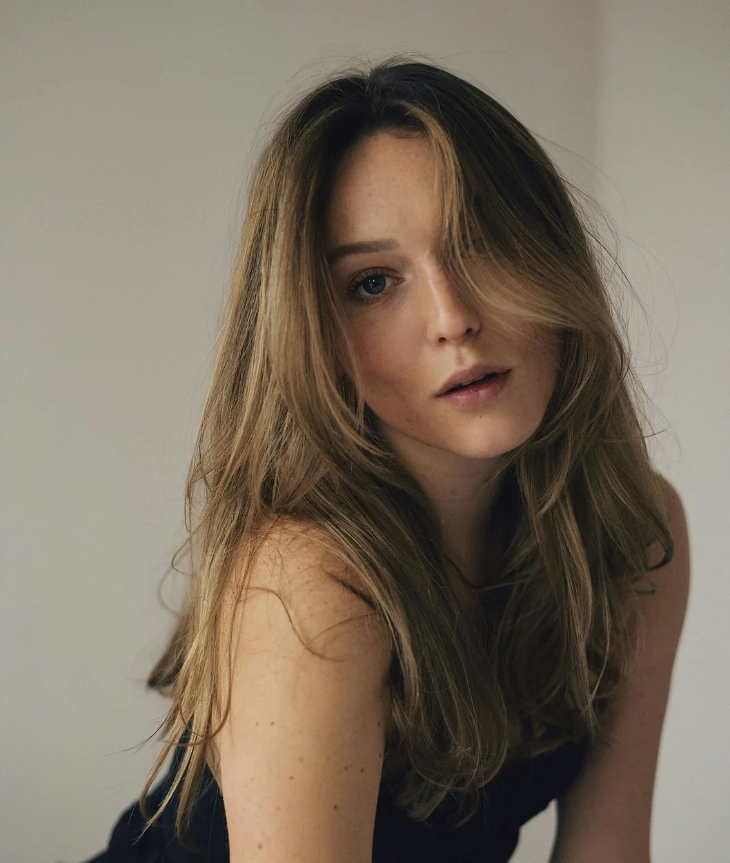 A young woman with long, wavy, light brown hair and freckles looking at the camera with a neutral expression, against a plain background.