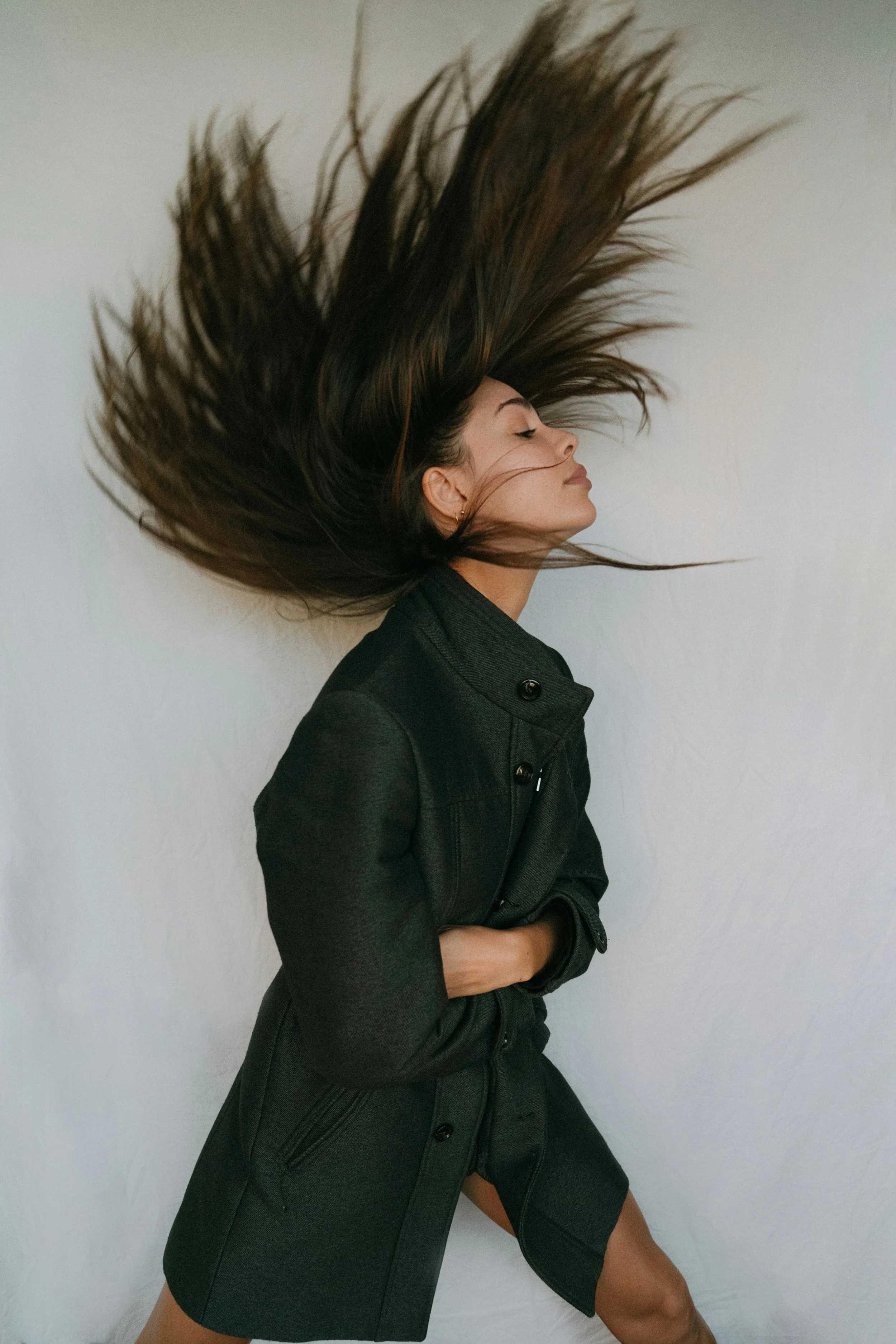 A woman with long hair is flipping her hair and standing against a plain white background.