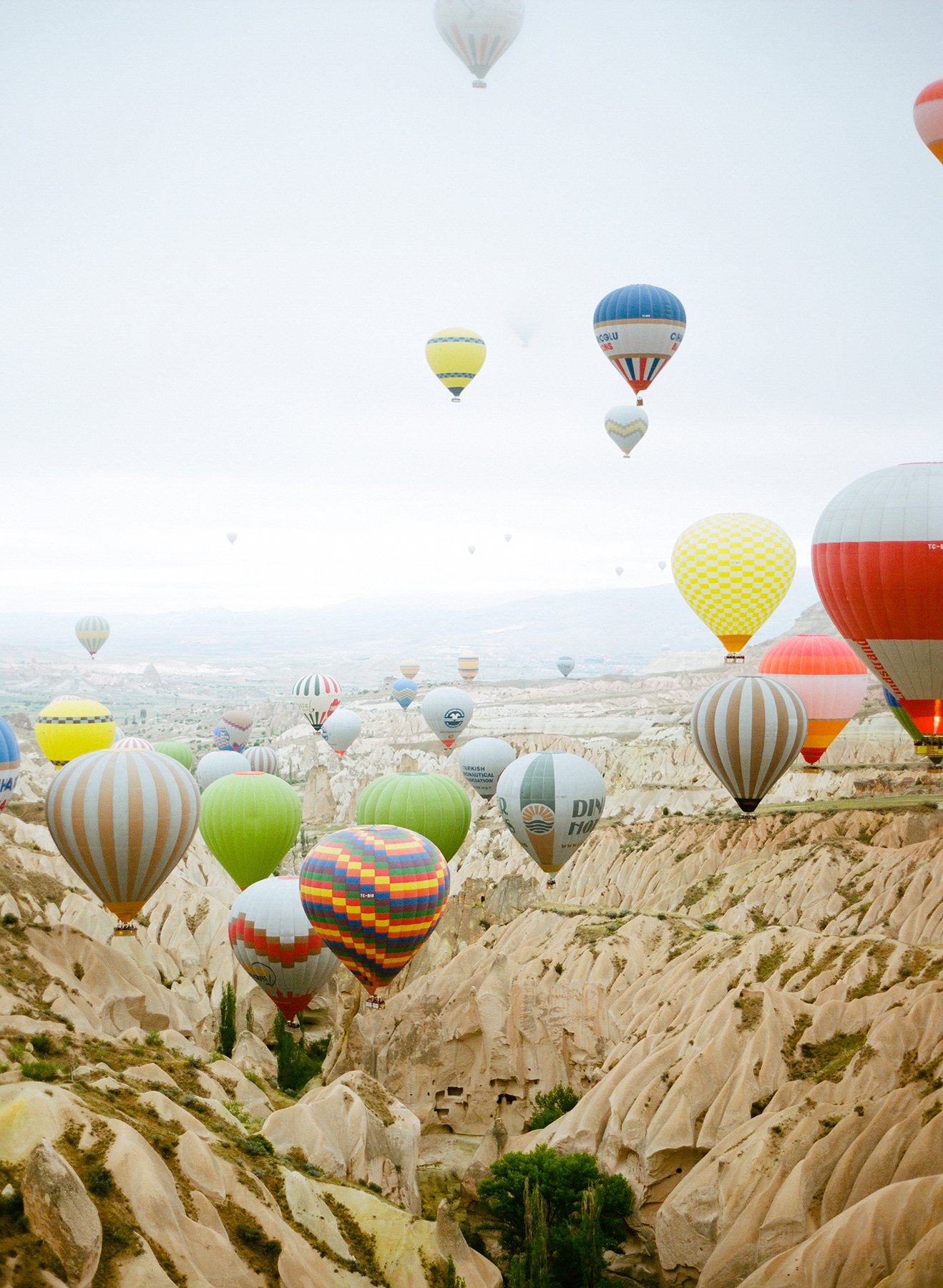 Multiple colorful hot air balloons floating over a valley with unique rock formations.