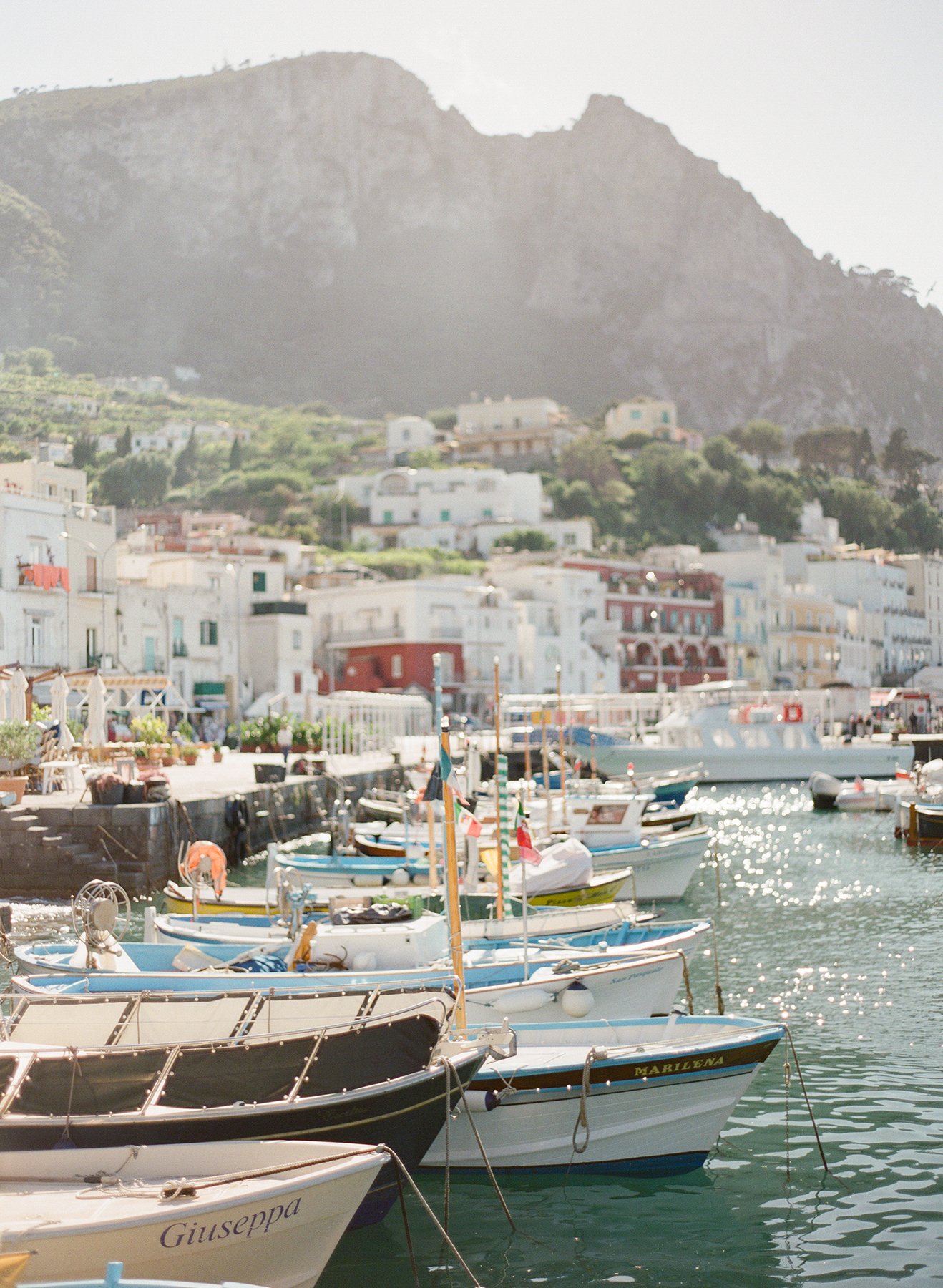 Boats docked in a harbor with colorful buildings and a mountainous landscape in the background.