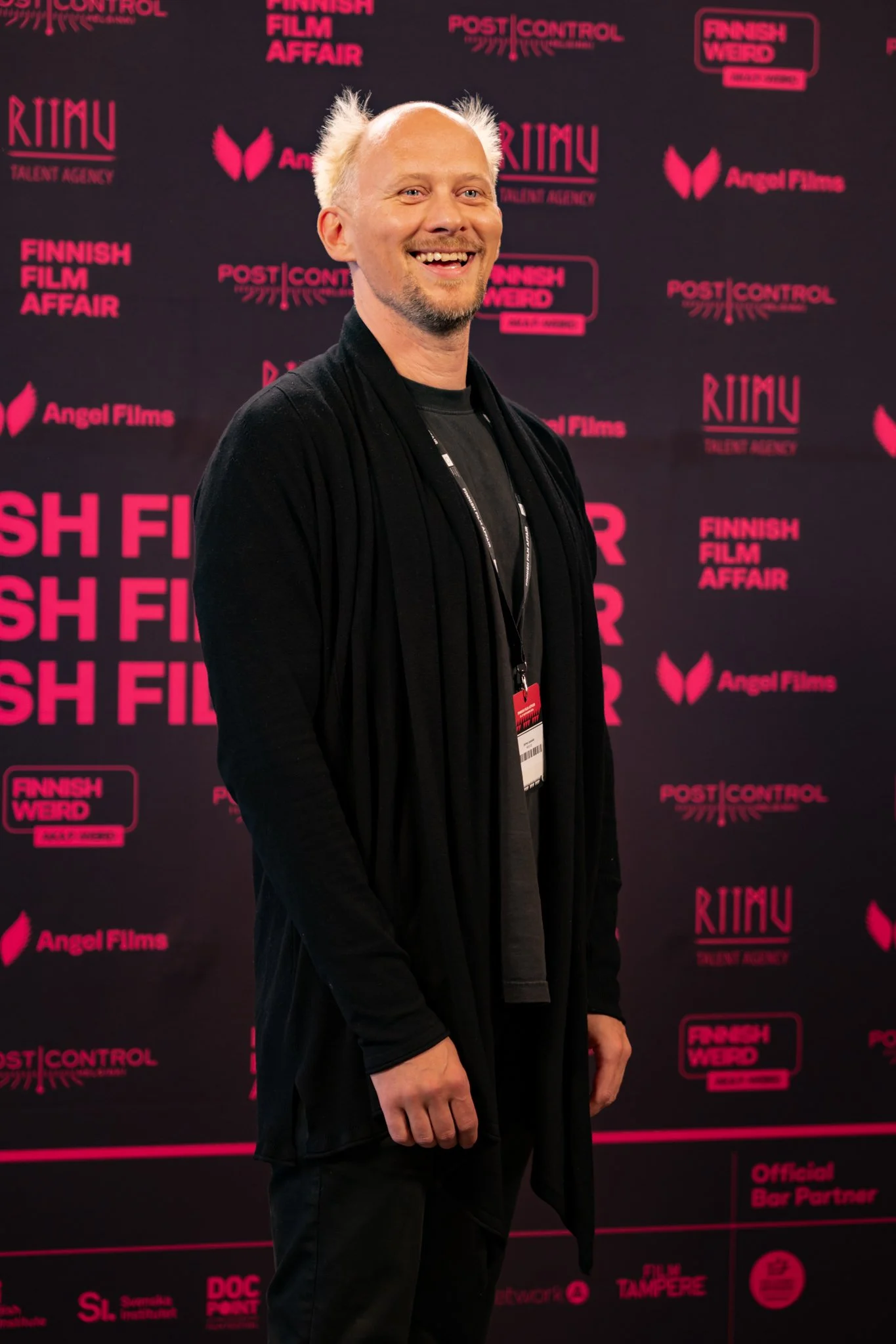 Man smiling at a film event, standing in front of a dark pink and black backdrop with logos and text including 'Finnish Film Affair' and 'Angel Films'.