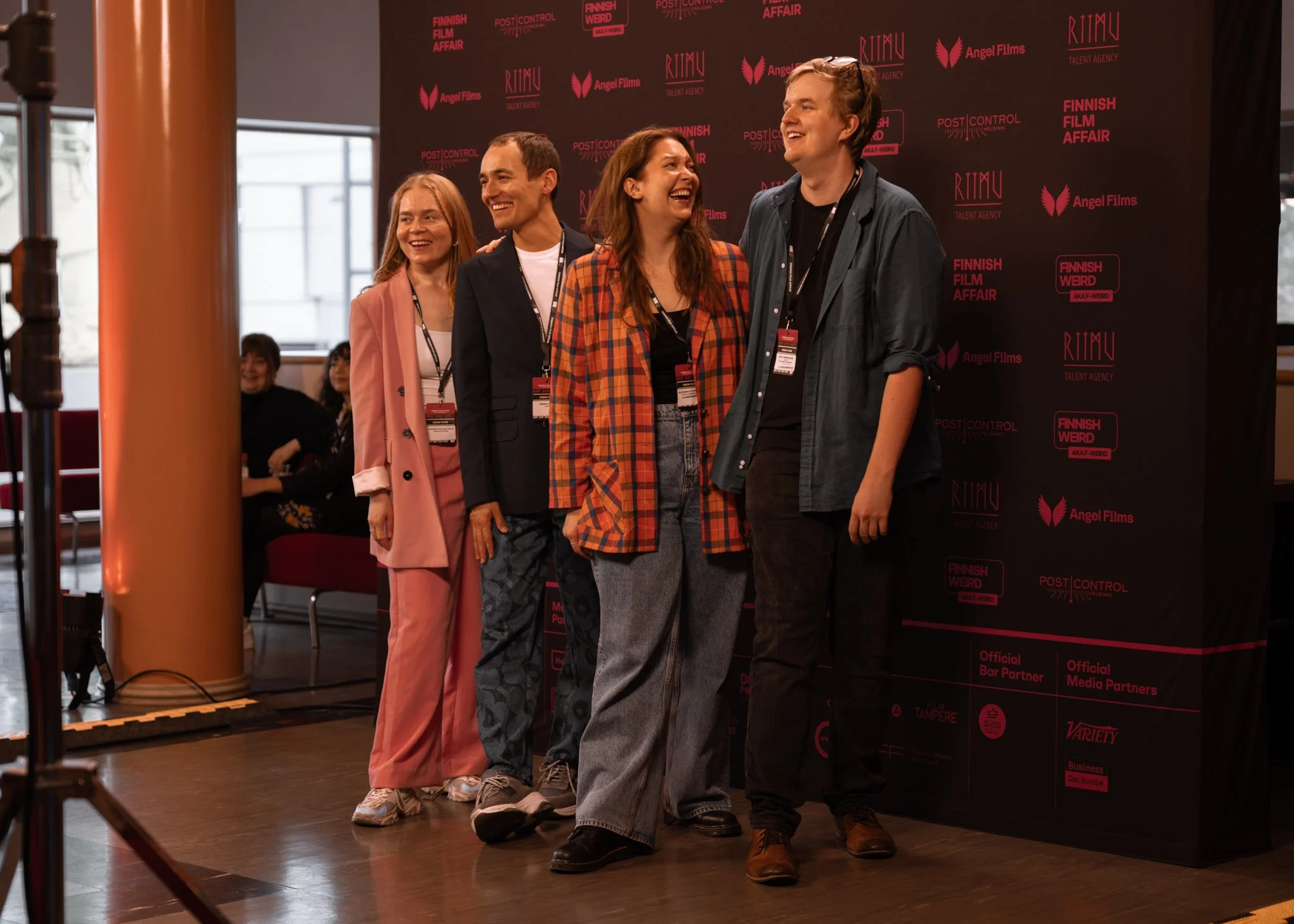 Group of five people smiling and posing together at an event, standing in front of a black backdrop with red and pink logos and text.