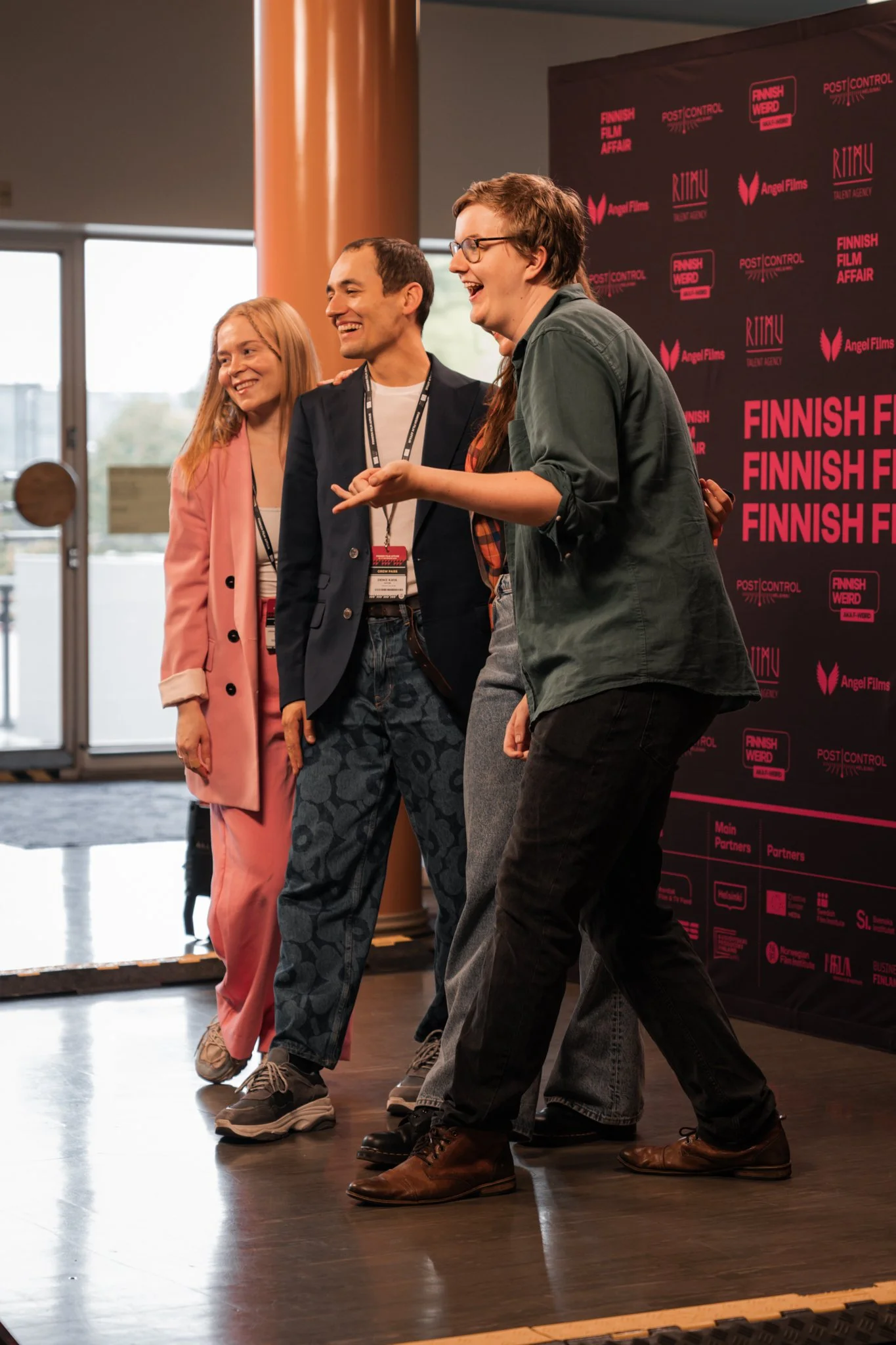 Four individuals standing and conversing at a Finnish film event, smiling, with a black event backdrop featuring pink and white text and logos.