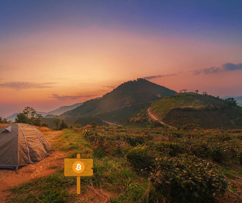 Tent on a grassy field with a Bitcoin symbol sign, hills and a colorful sunset sky in the background.