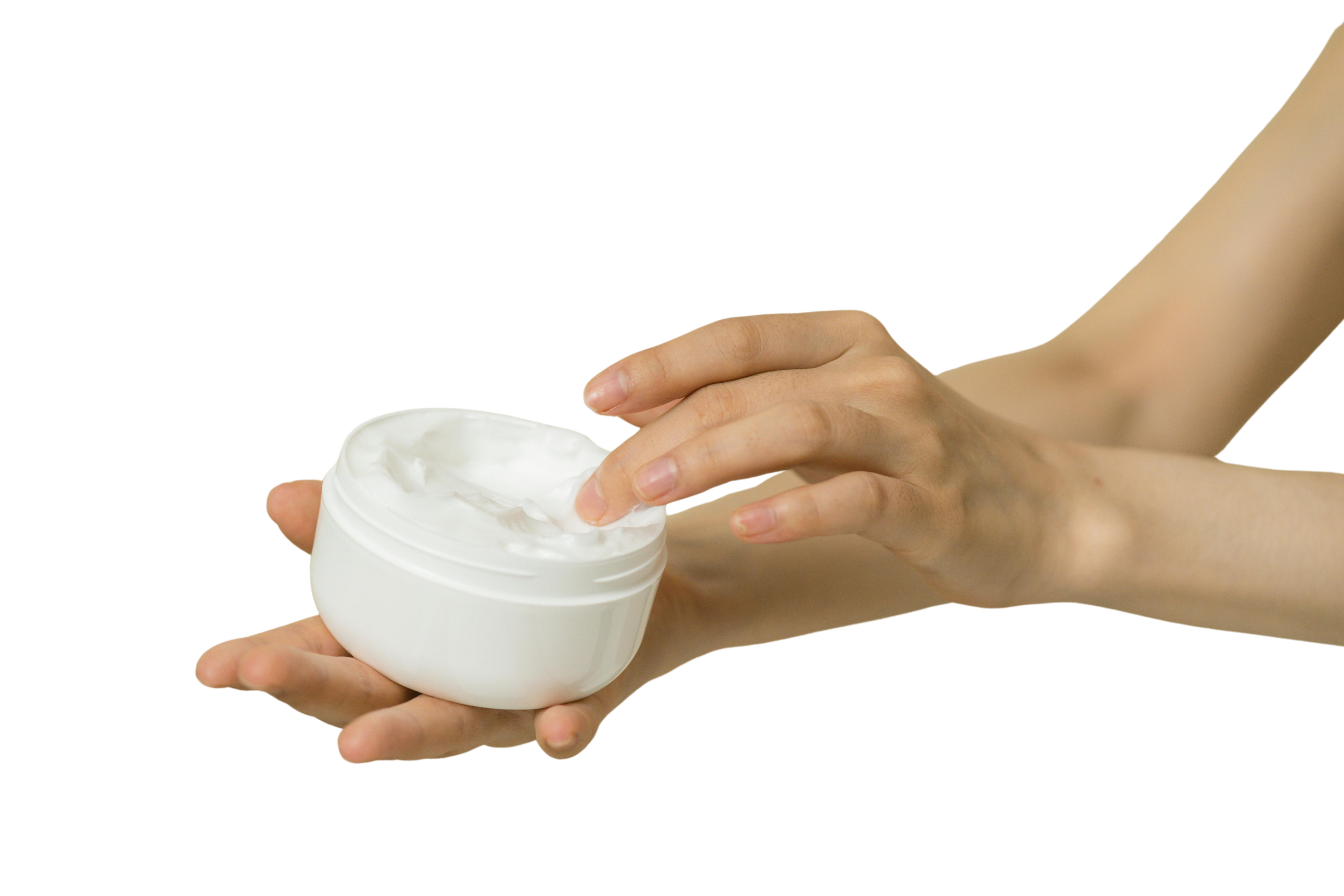 Person scooping white cream or lotion from a white jar.