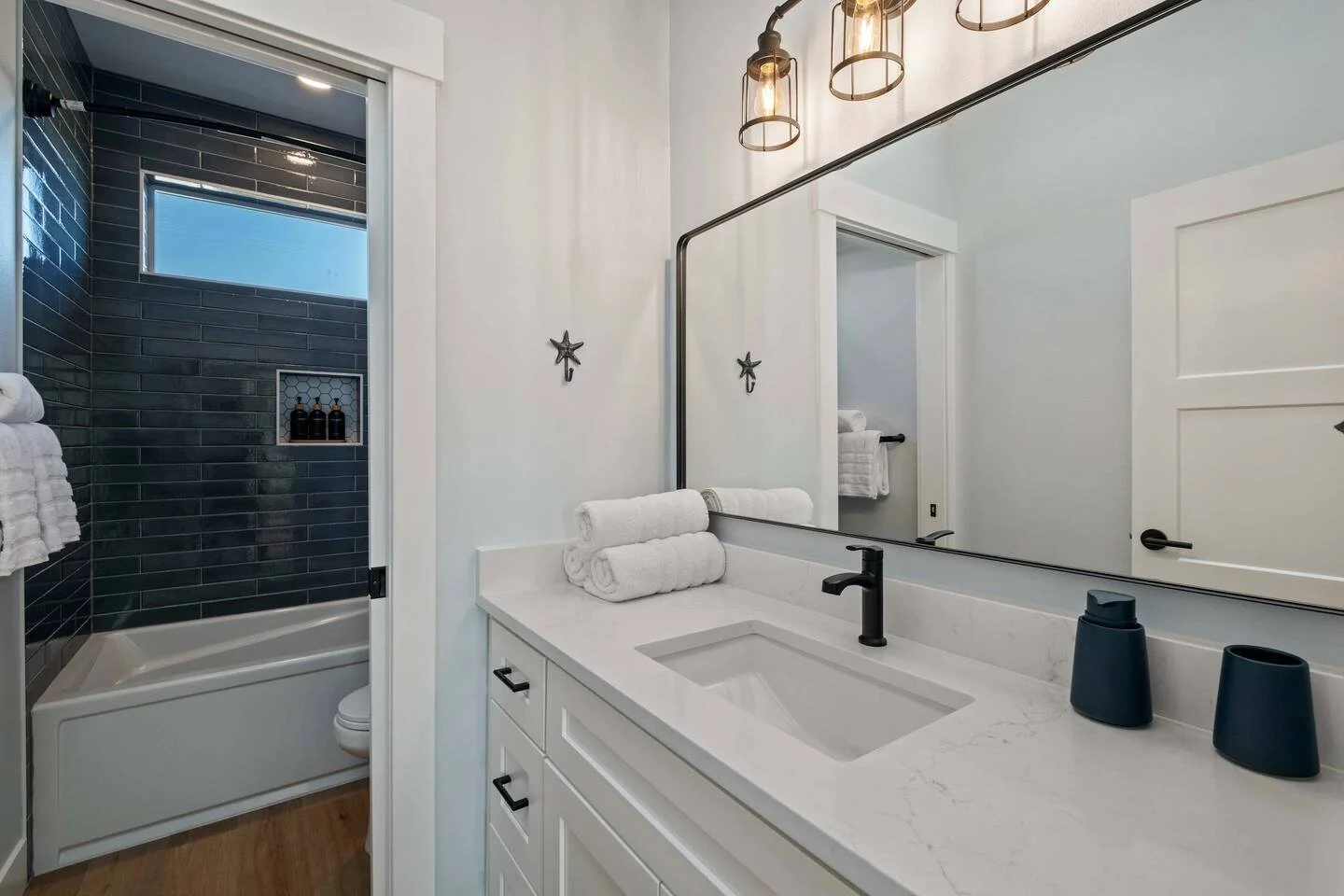Modern bathroom with white vanity, black faucet, large mirror, white towels, and a separate shower with black tiles and a small window.