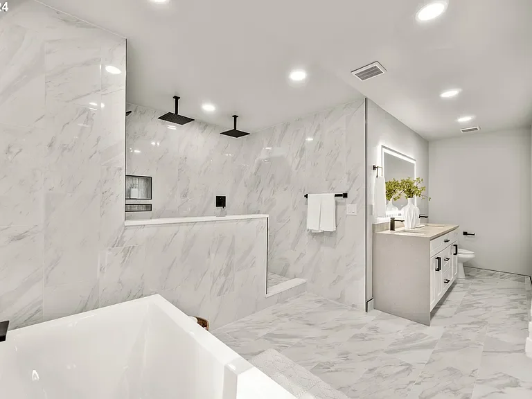Modern bathroom with white marble walls and floors, a large bathtub, a walk-in shower with black fixtures, a white vanity with a mirror, and a small plant on the counter.