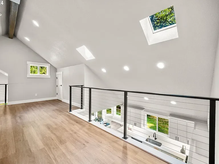 Bright modern open-space interior with white walls, wood flooring, multiple skylights, and windows showing greenery outside.