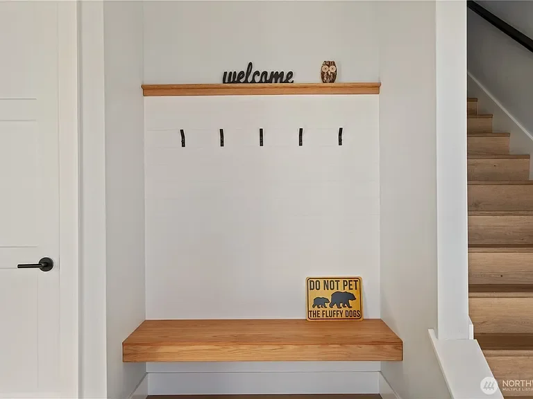 Entryway wall with a wooden bench, coat hooks, a wooden shelf with 'welcome' decor, and a sign that says 'Do not pet the fluffy dogs'.