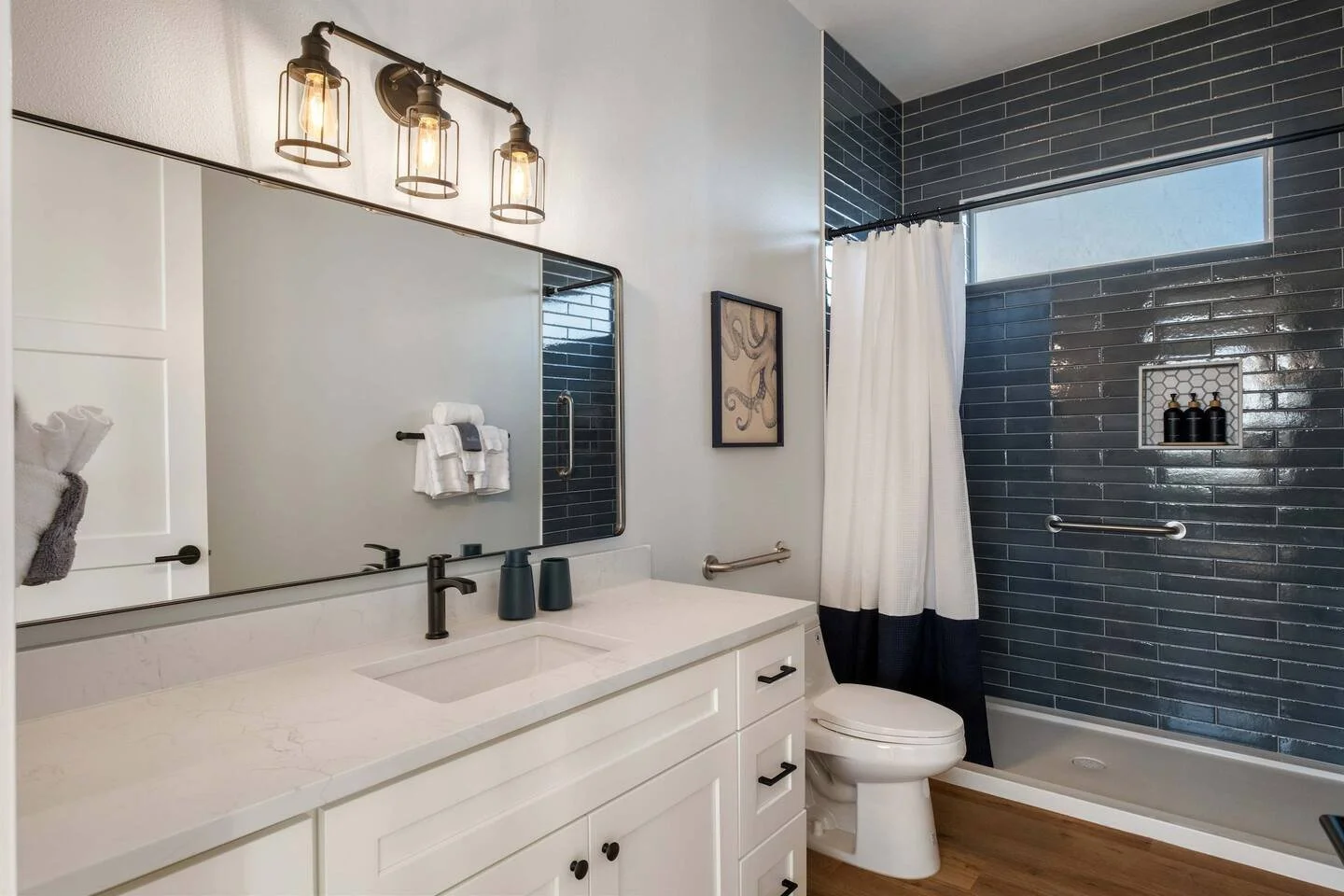 Modern bathroom with white vanity, black fixtures, navy tile shower with window, white curtain, and wooden floor.
