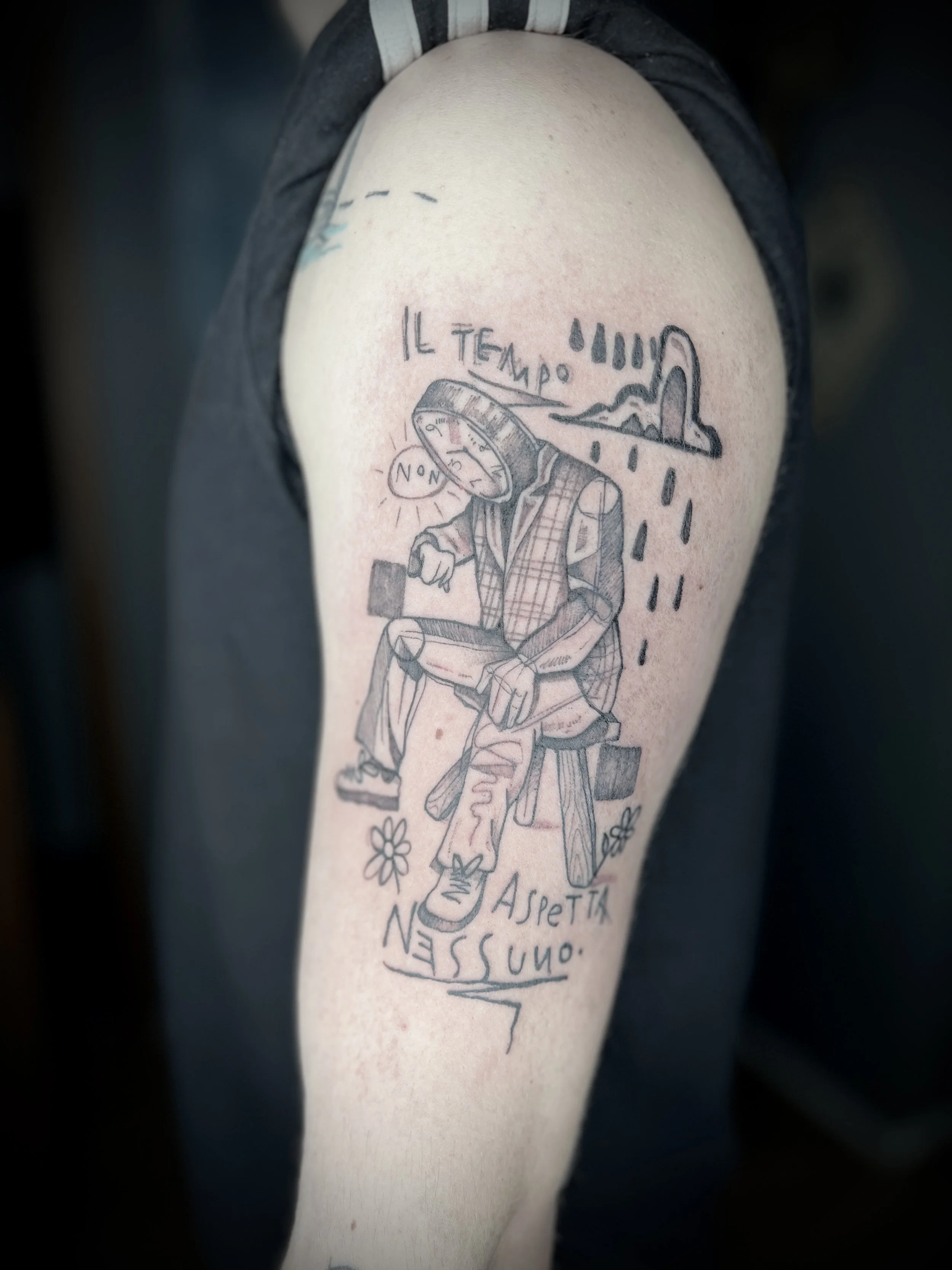 Tatuaggio su braccio di un uomo che mostra un uomo seduto con un quadrante come testa, sotto un ombrello sotto la pioggia, con scritte in italiano 'Il tempo' e 'aspettano nessuno'.