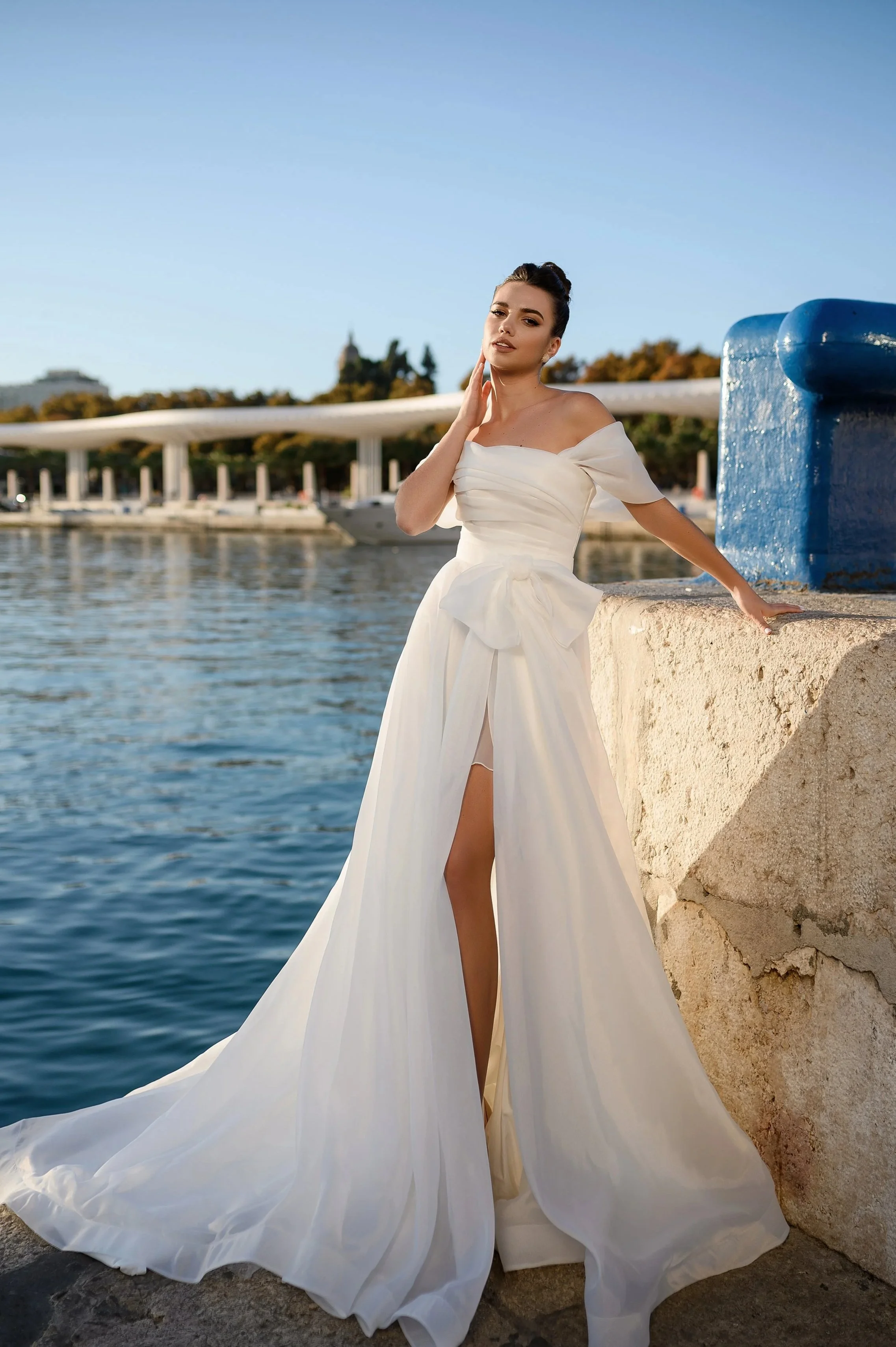 Femme portant une robe de mariée blanche près de l'eau, près d'un quai.