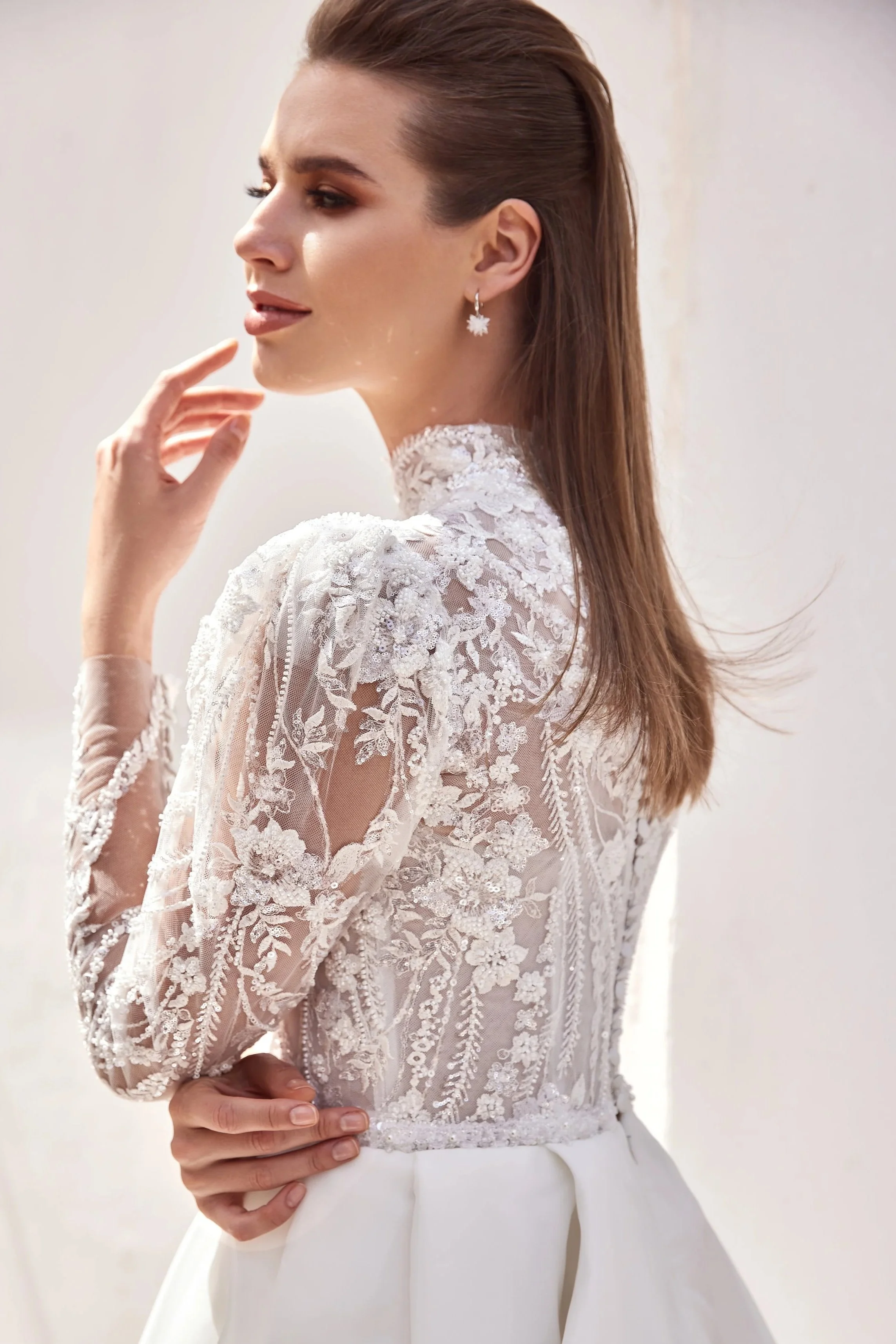 Une femme vêtue d'une robe de mariée en dentelle blanche, regardant vers la gauche, avec des boucles d'oreilles en forme d'étoile.