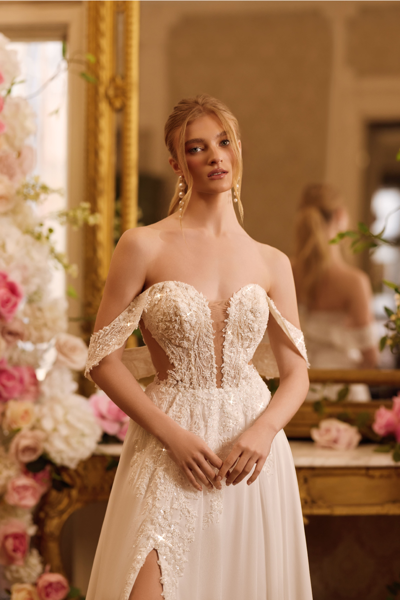 Femme portant une robe de mariée élégante avec des détails en dentelle et un corsage bustier, debout dans une pièce décorée avec des fleurs.