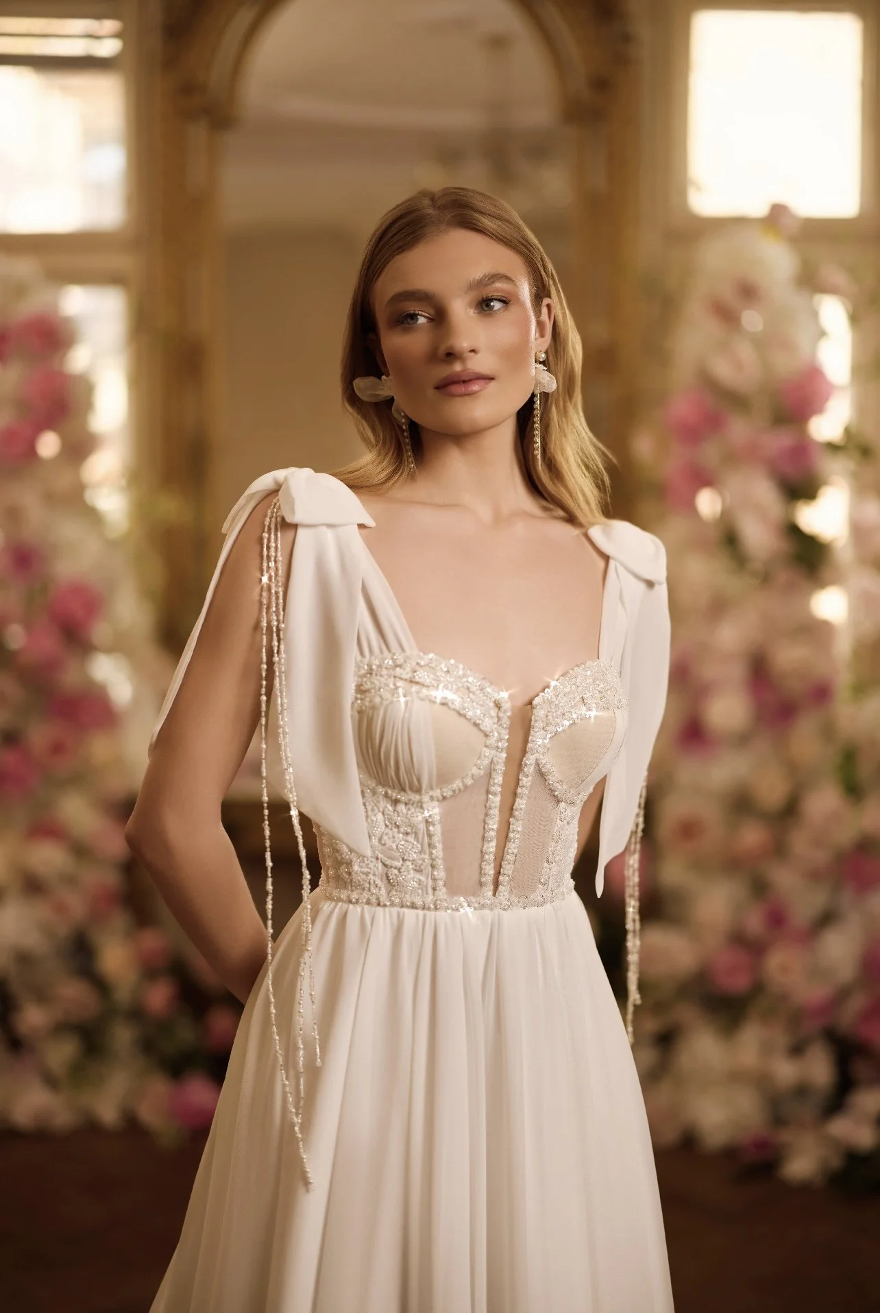 Femme portant une robe de mariée avec des détails en perles et broderies, dans un décor floral et élégant.