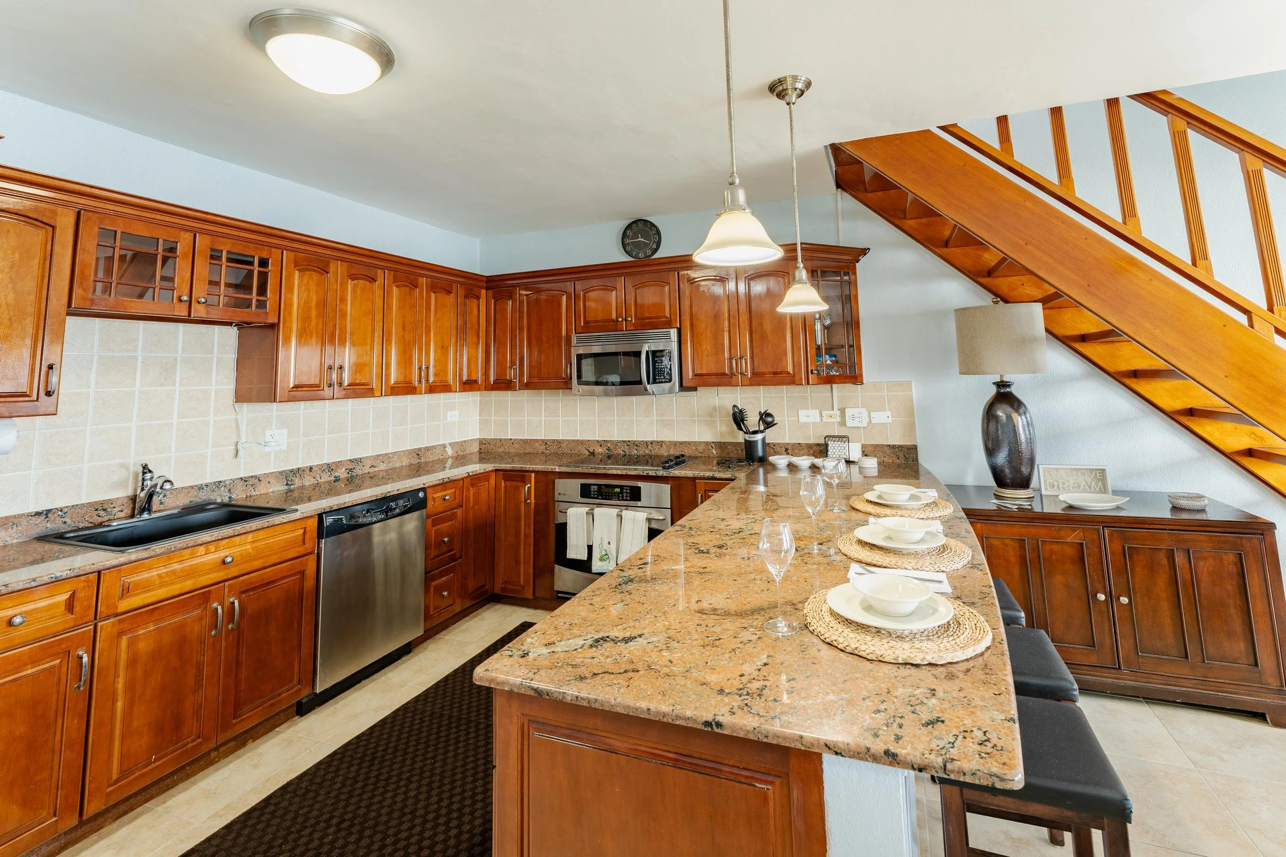 Kitchen with wooden cabinets, granite countertop, stainless steel appliances, and a breakfast bar with place settings and glasses.