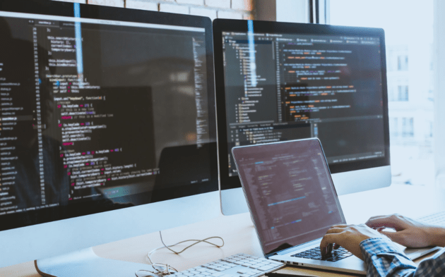 Person typing on a Dell laptop beside a MacBook Air on a desk.