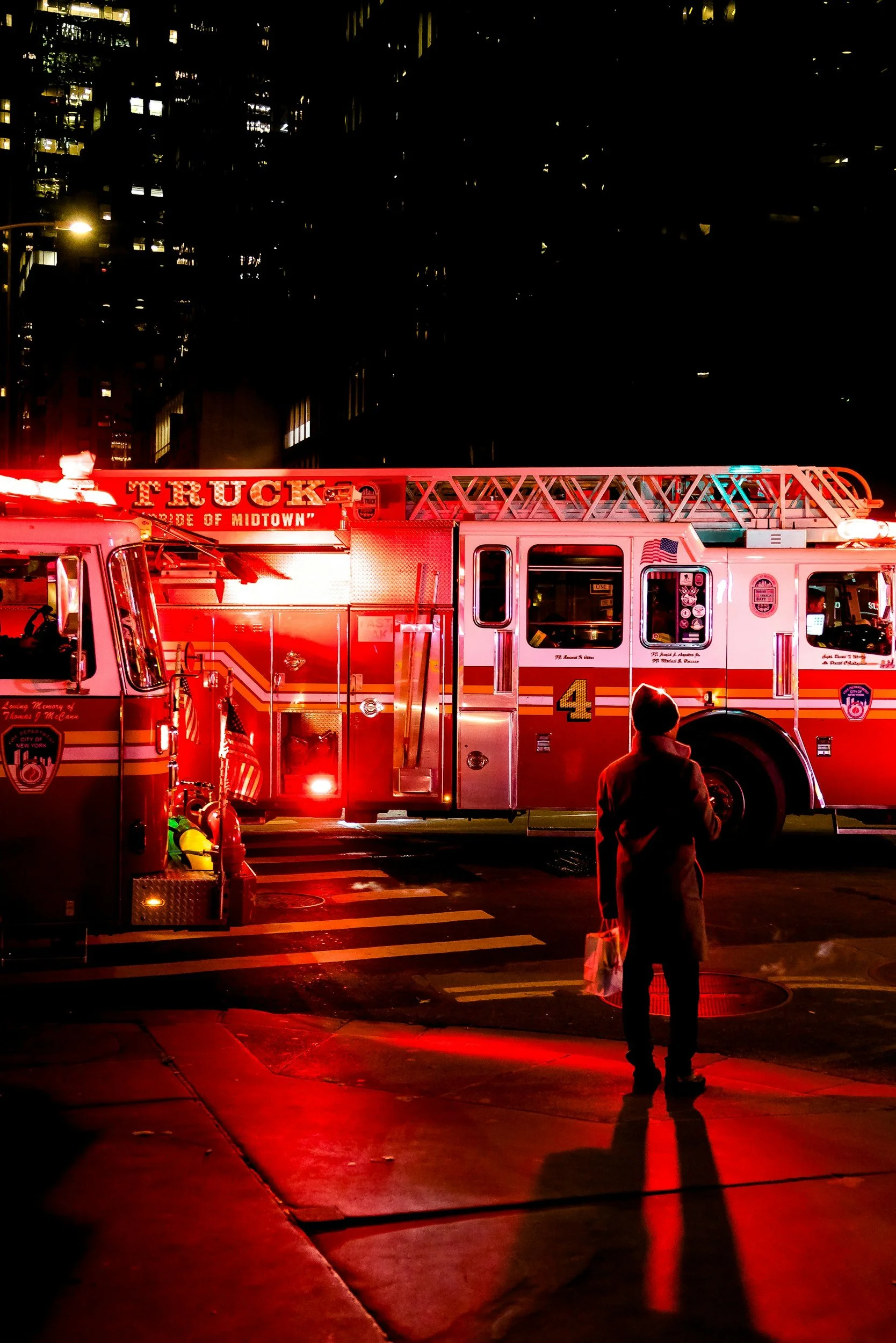 Fire truck at night with open equipment compartment, showing hoses and gauges, surrounded by firefighters.