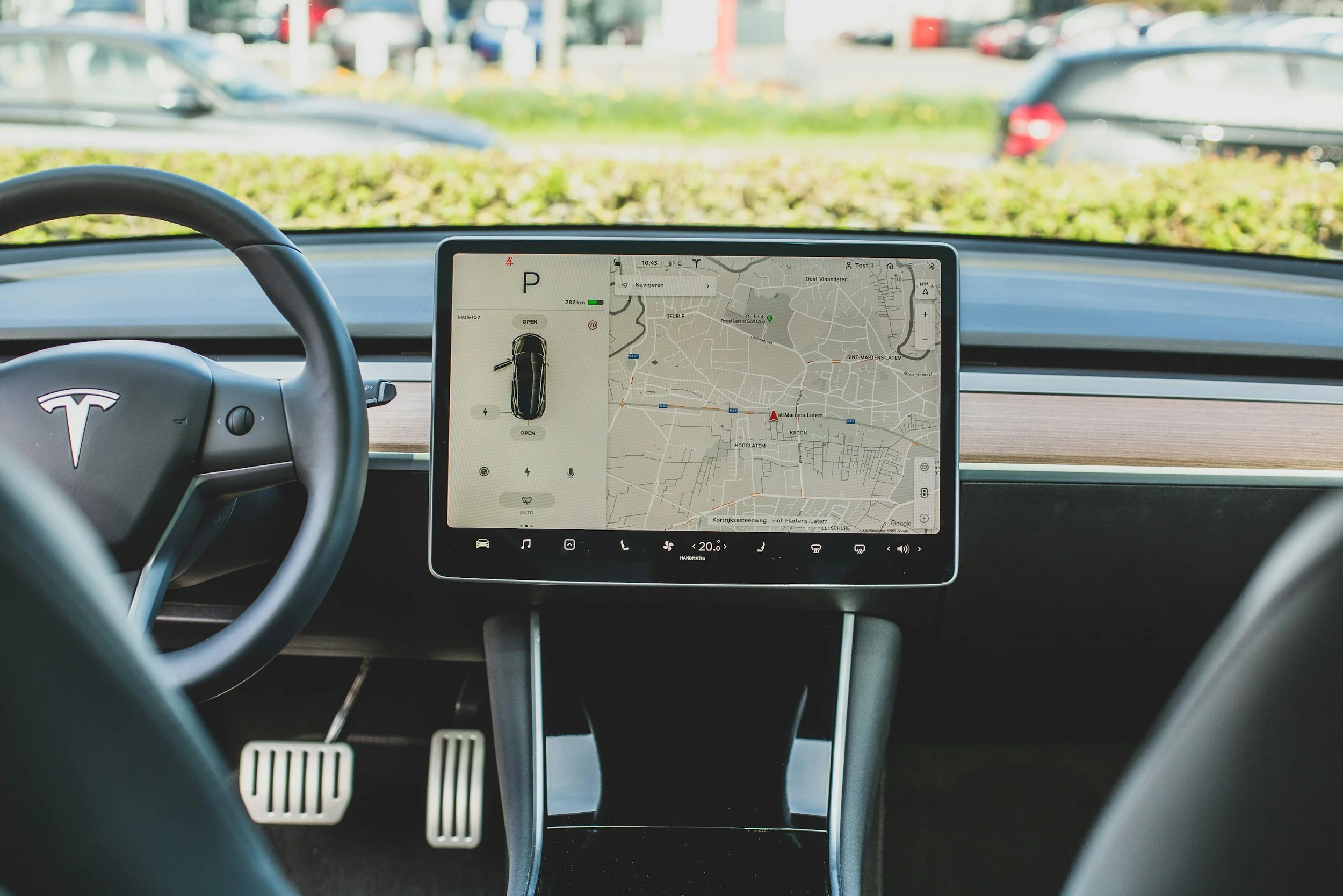 Person using Tesla touchscreen dashboard, displaying navigation map and vehicle controls, while driving.