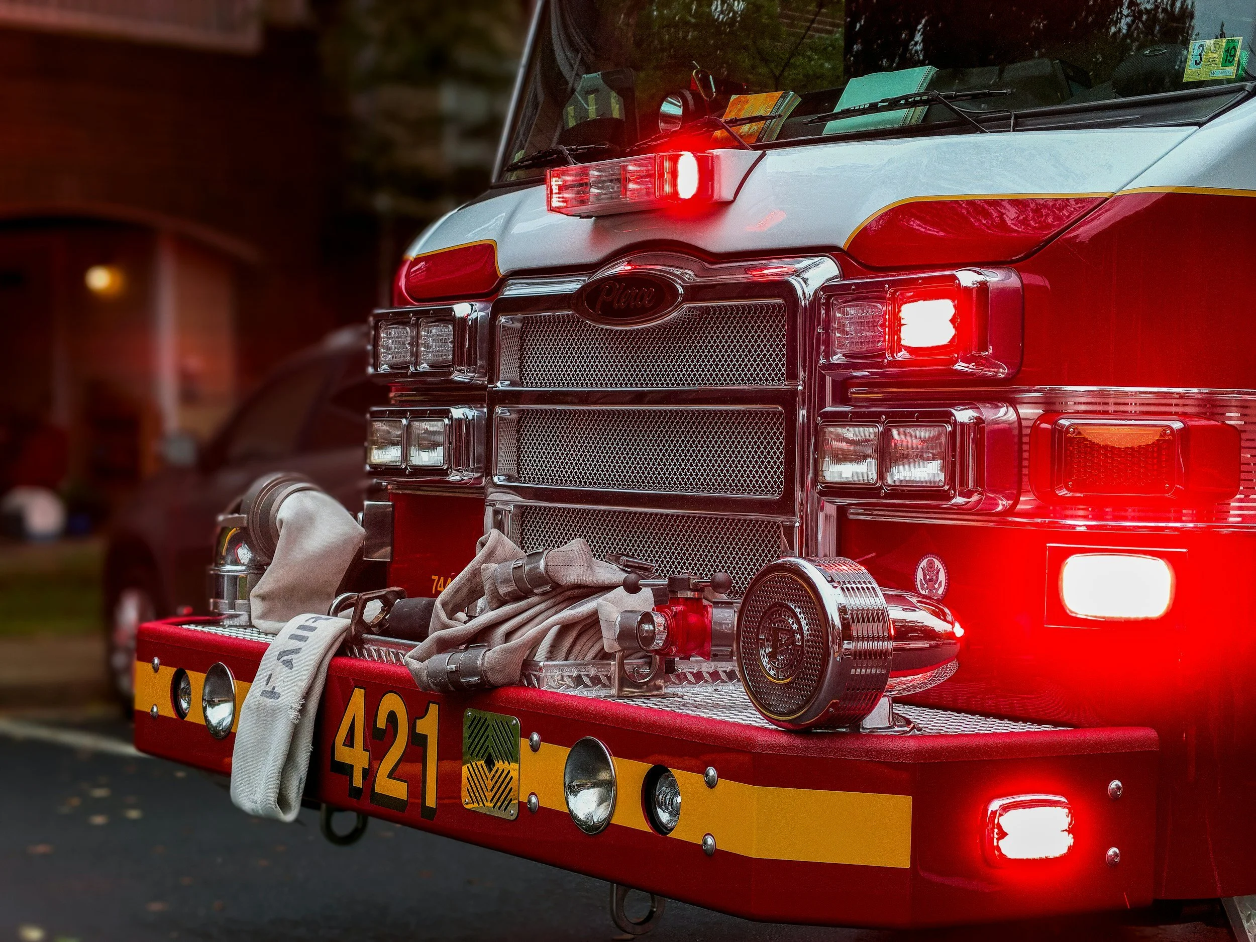 Front view of a red fire truck with lights on, featuring a hose and equipment on the bumper, marked with the number 421.
