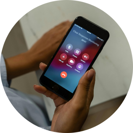 Person holding a smartphone during a call, with the screen showing a call in progress with Clear Response Monitoring and options for call functions.