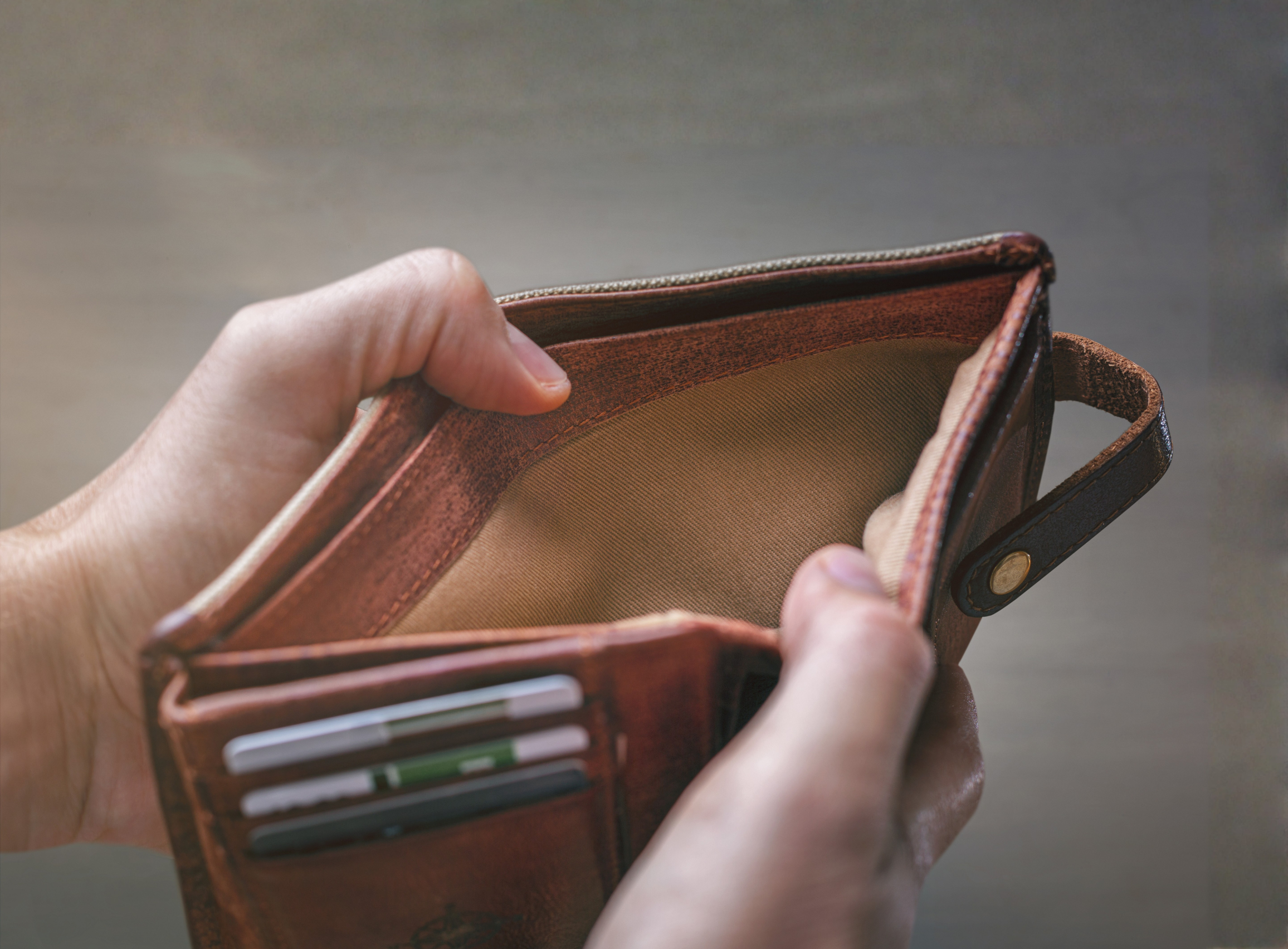 A person holds an open brown leather wallet with multiple card slots and a cash compartment, showing several colorful cards inside.