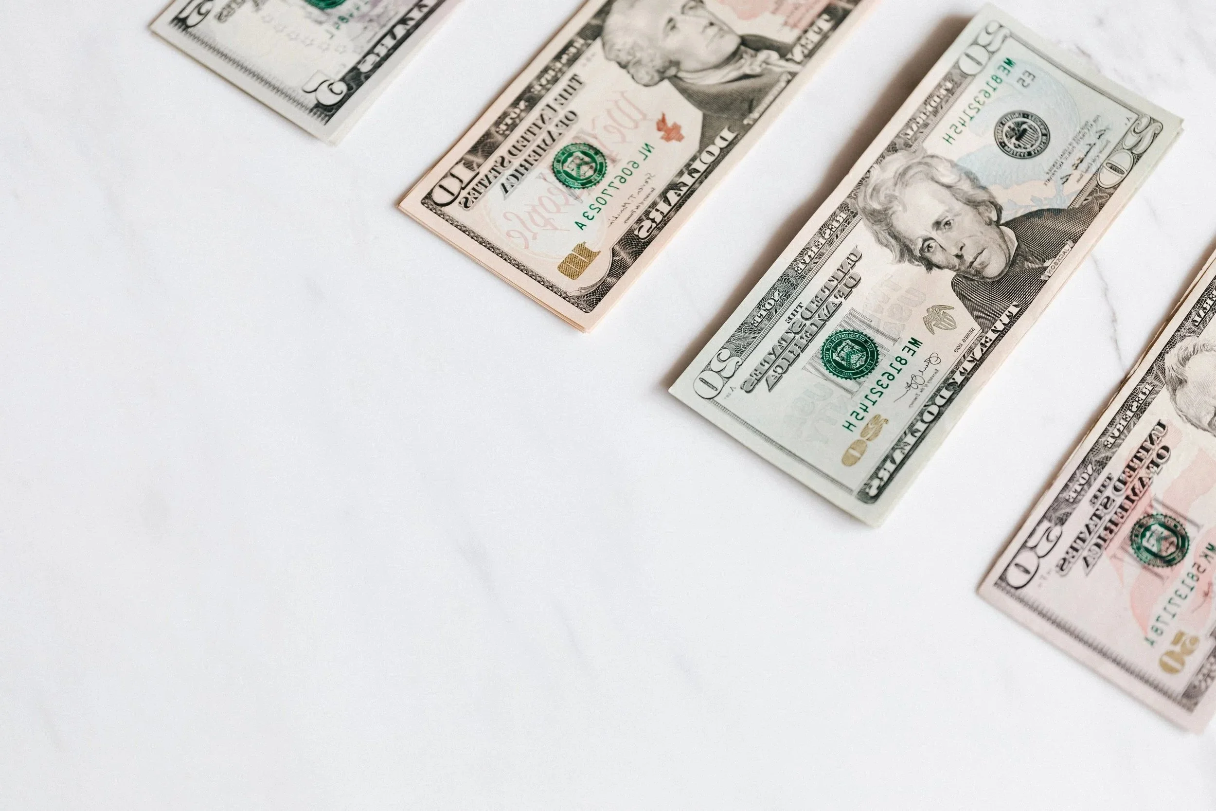 Multiple US dollar bills, including $50 and $20 denominations, arranged on a white surface.