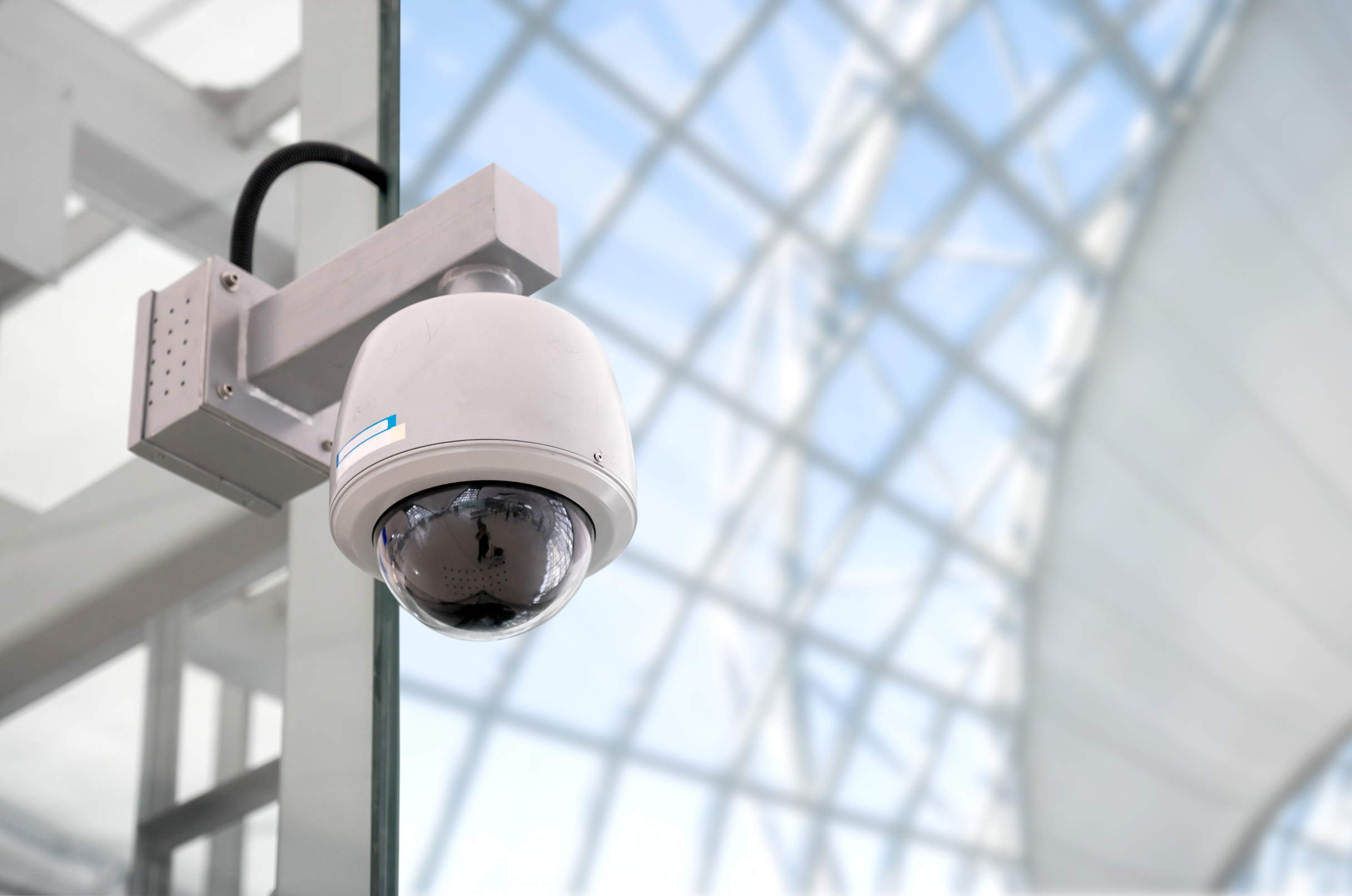 Close-up of a security camera lens on a metallic surface with reflected cityscape.