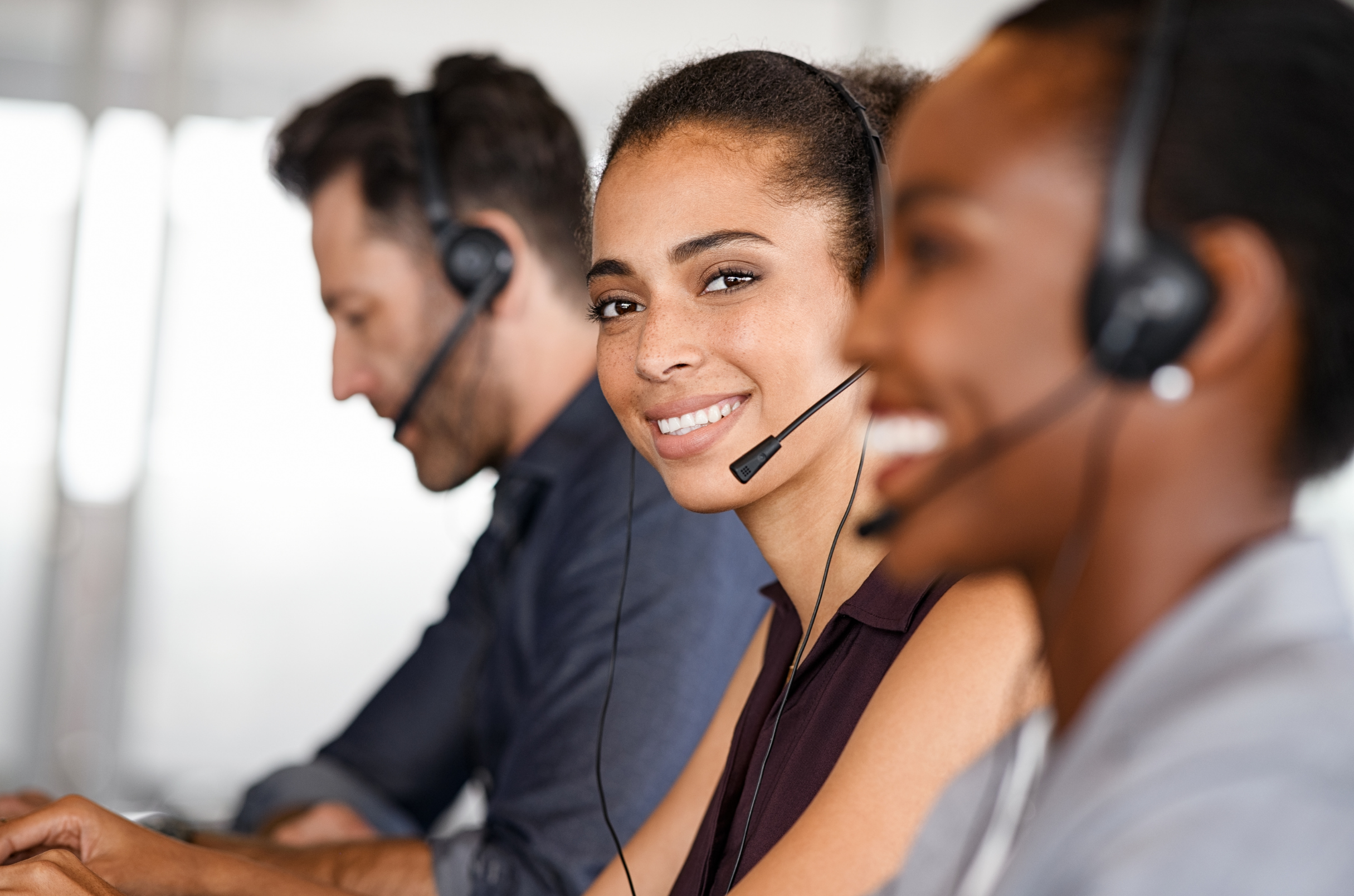 Two call center employees wearing headsets, sitting at desks with computers, in a modern office environment.