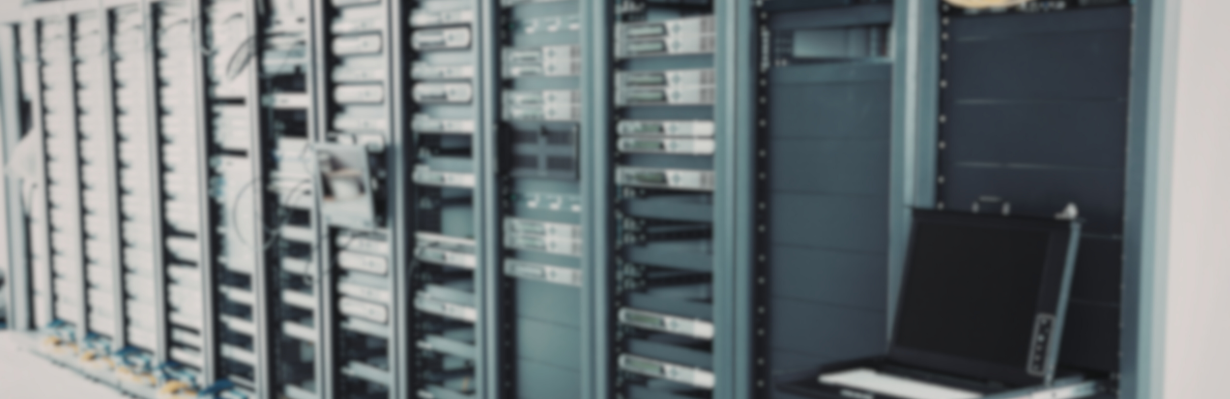 A blurred image of server racks in a data center with a laptop on the floor.
