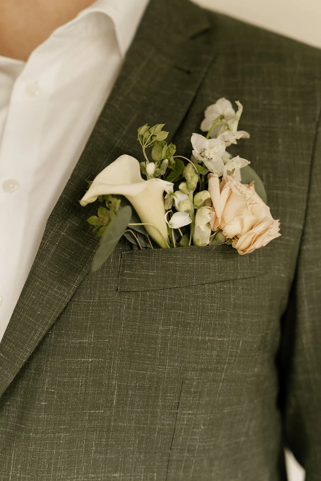 Close-up of a jacket pocket with a boutonniere of white and pale peach flowers on a dark plaid suit.