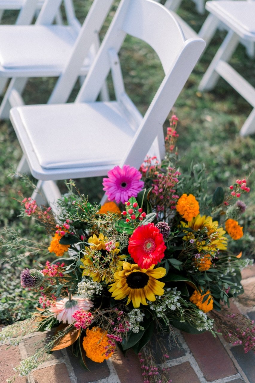 White chairs with a colorful flower arrangement on a brick surface, outdoor setting.