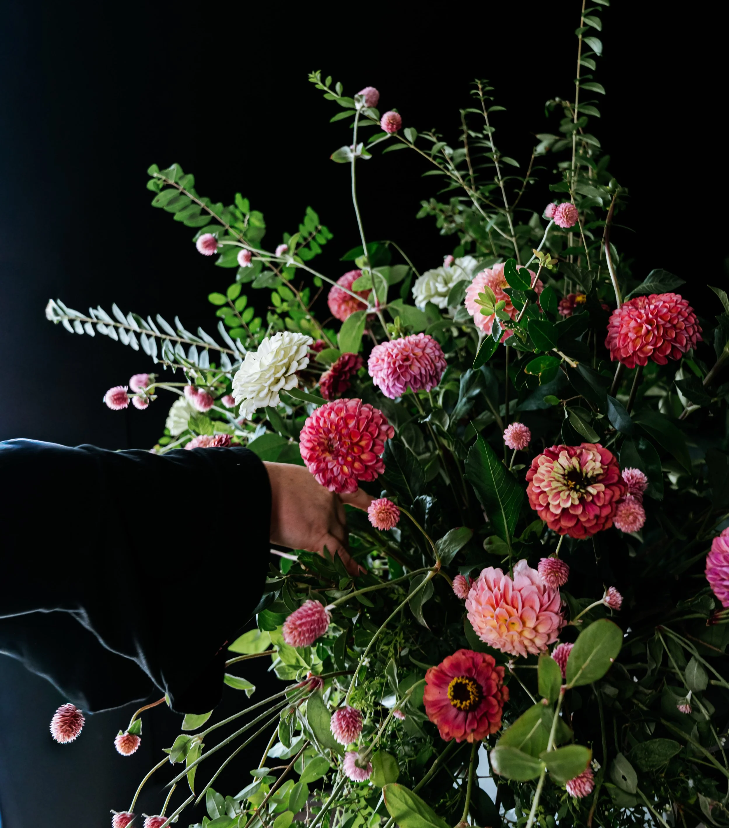 A person's hand touching a bouquet of pink and white flowers against a dark background.