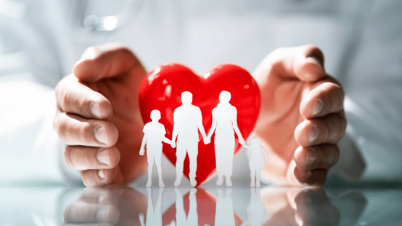 Hands holding a red heart with paper cutouts of a family, symbolizing family and healthcare support.