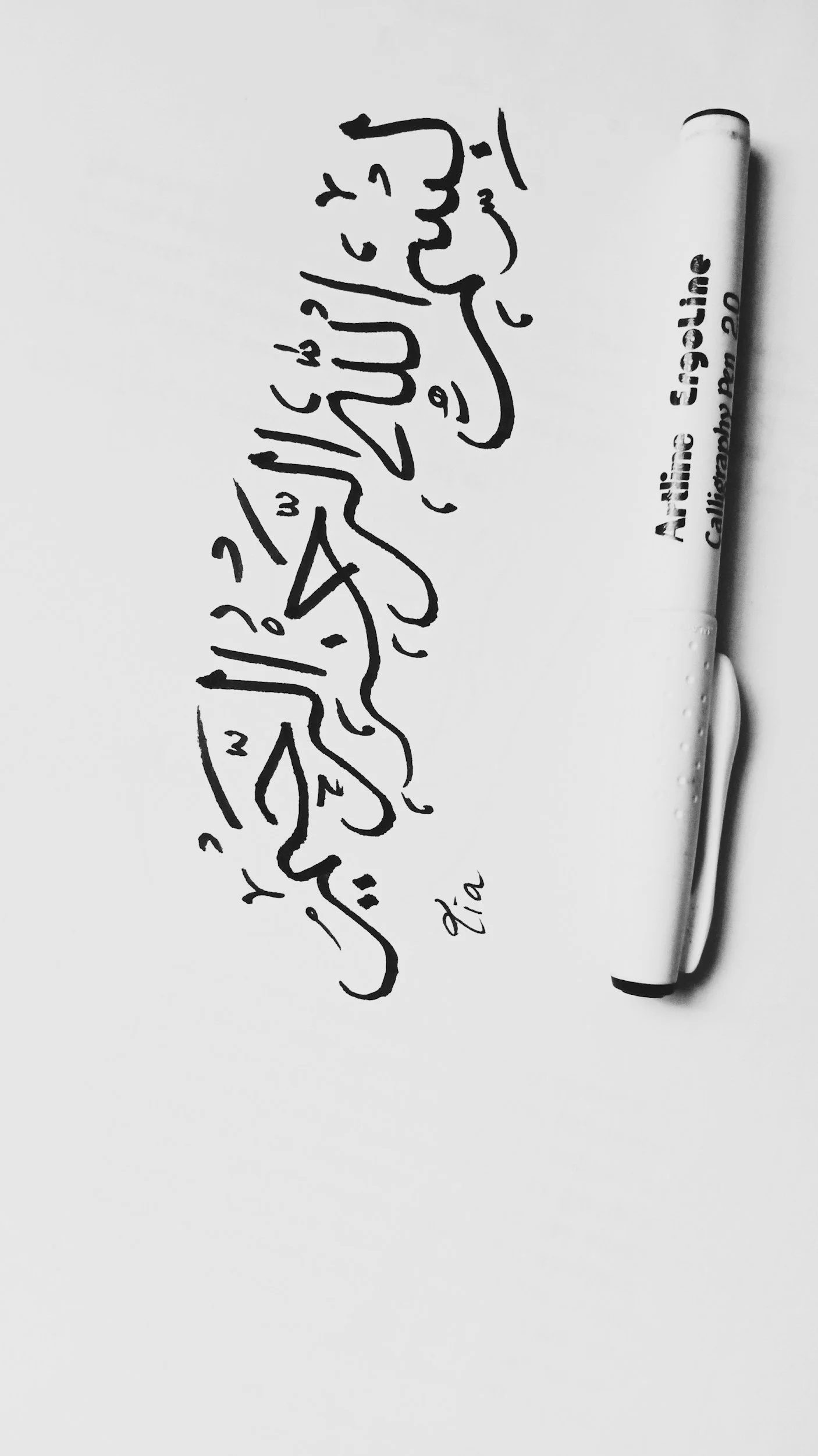 Black marker writing in Arabic on a white background, with a white marker pen beside it.