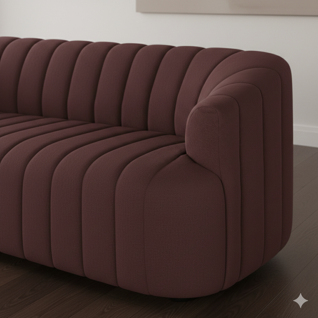 A maroon upholstered sofa with channel tufting, placed on a dark wooden floor against a white wall.