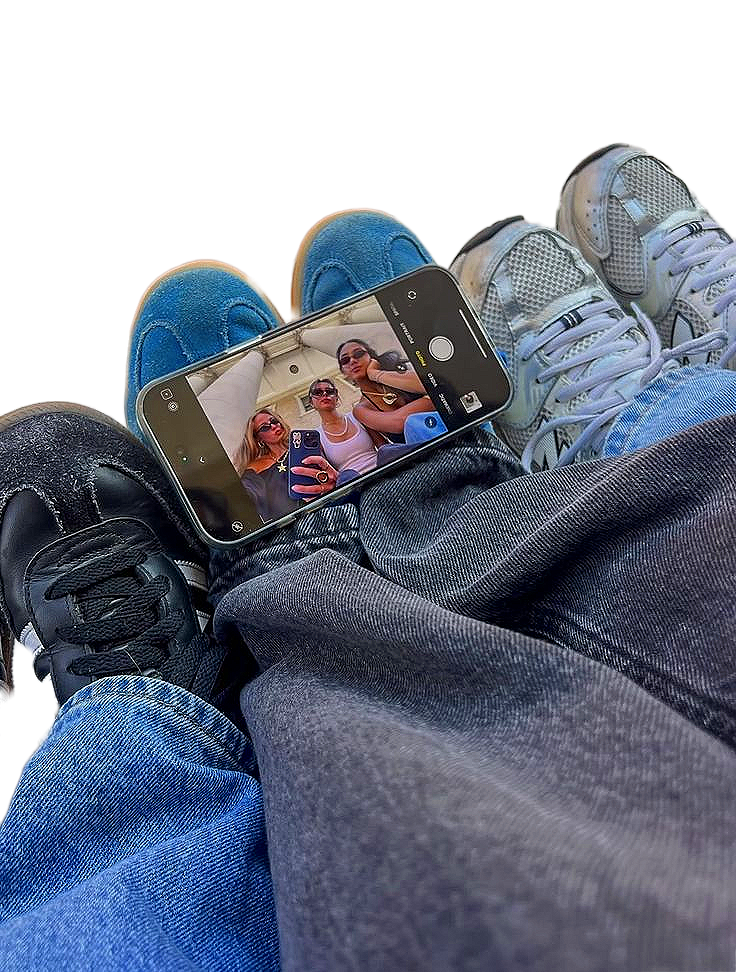 Photo of three women taking a selfie with a smartphone, with their legs and sneakers visible in the foreground.