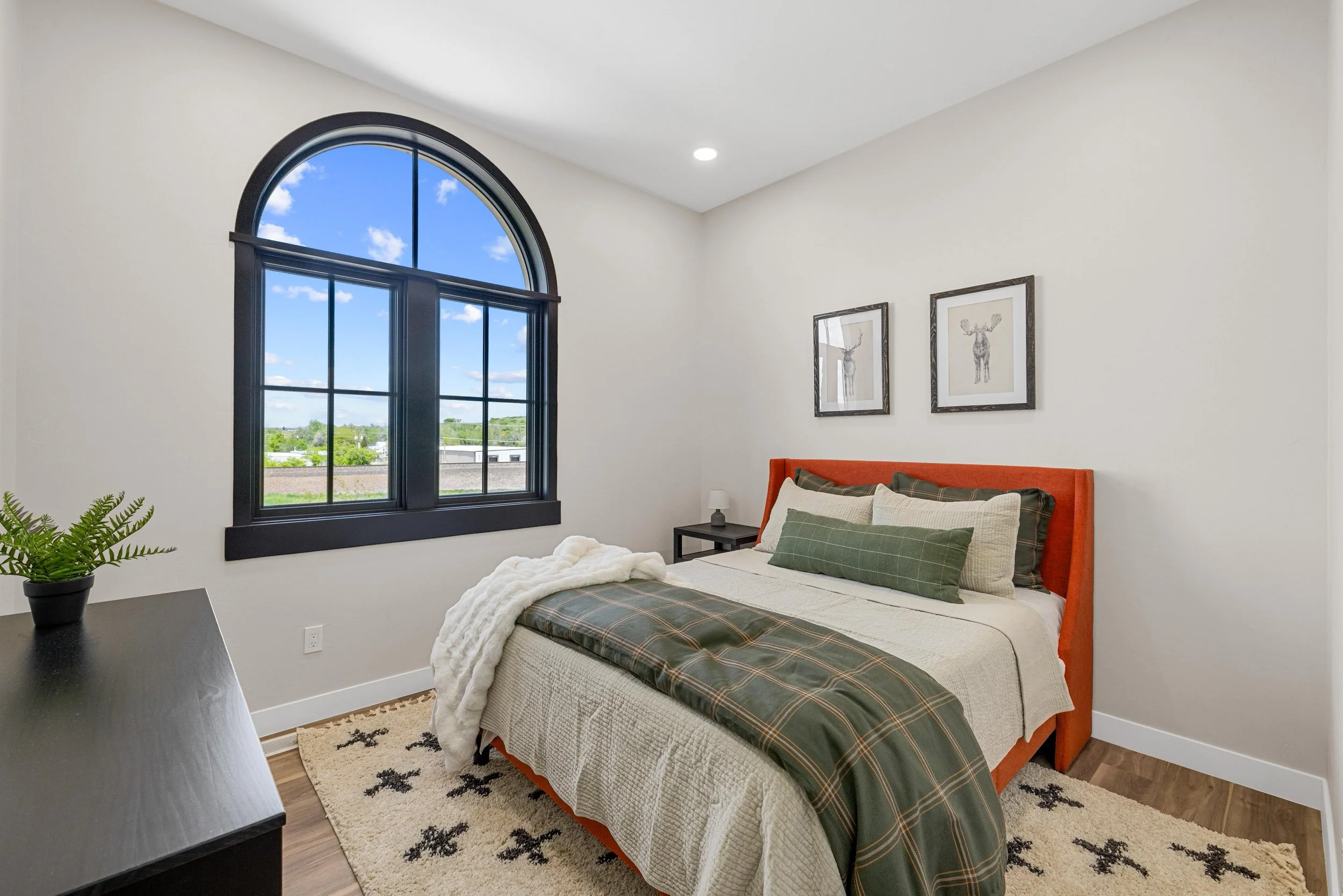 Primary bedroom in an Ice Haus Condo in Sheridan, Wyoming, that is for sale,  featuring an arched window, modern furnishings, and warm mountain-inspired decor.