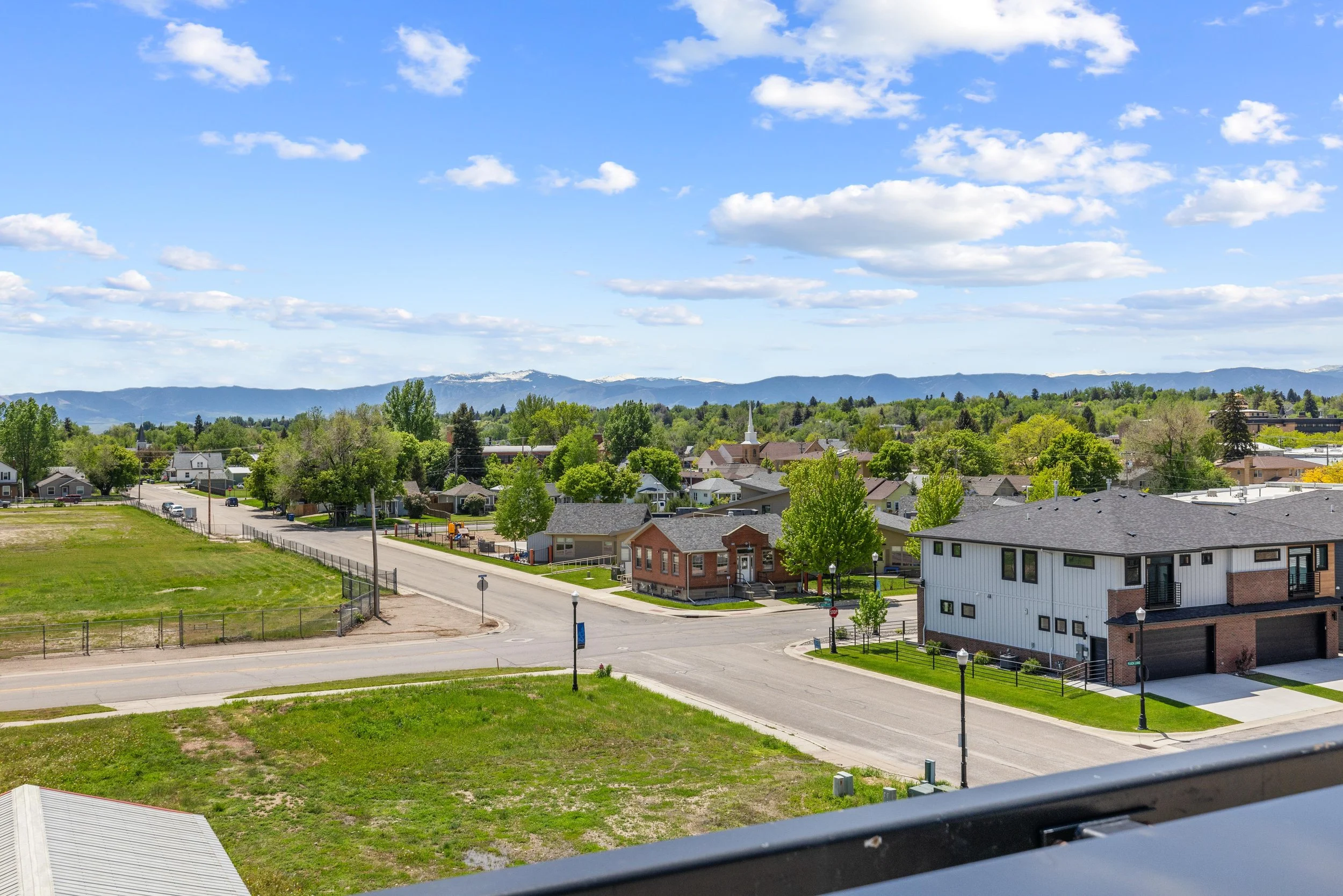 View of a suburban neighborhood with houses, trees, and mountains in the distance on a clear day with blue sky and clouds.