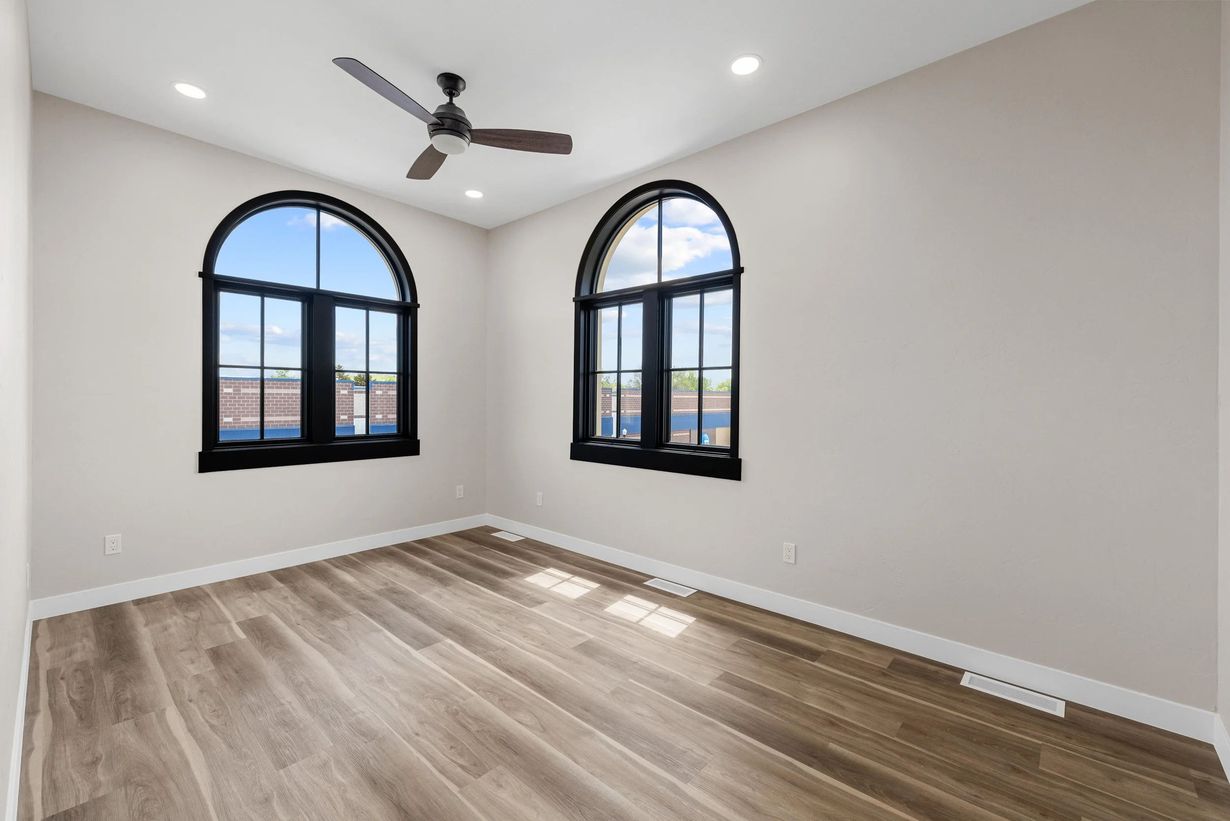 Empty room with two arched windows, a ceiling fan, hardwood floors, and ceiling lights.