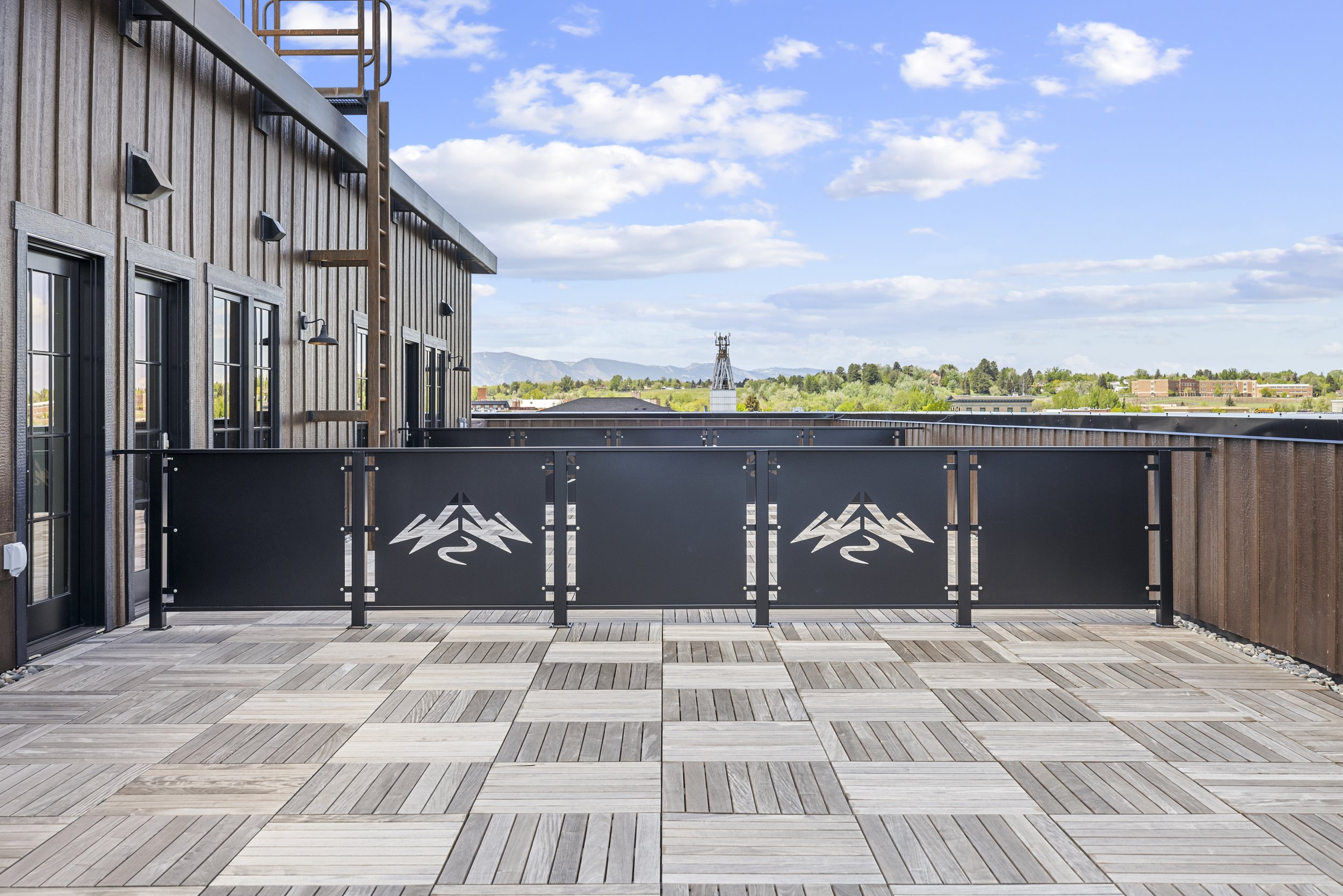 Rooftop terrace at Ice Haus Condos for sale in Sheridan, Wyoming featuring wood flooring, mountain-inspired railings, glass doors, and scenic Wyoming mountain views.