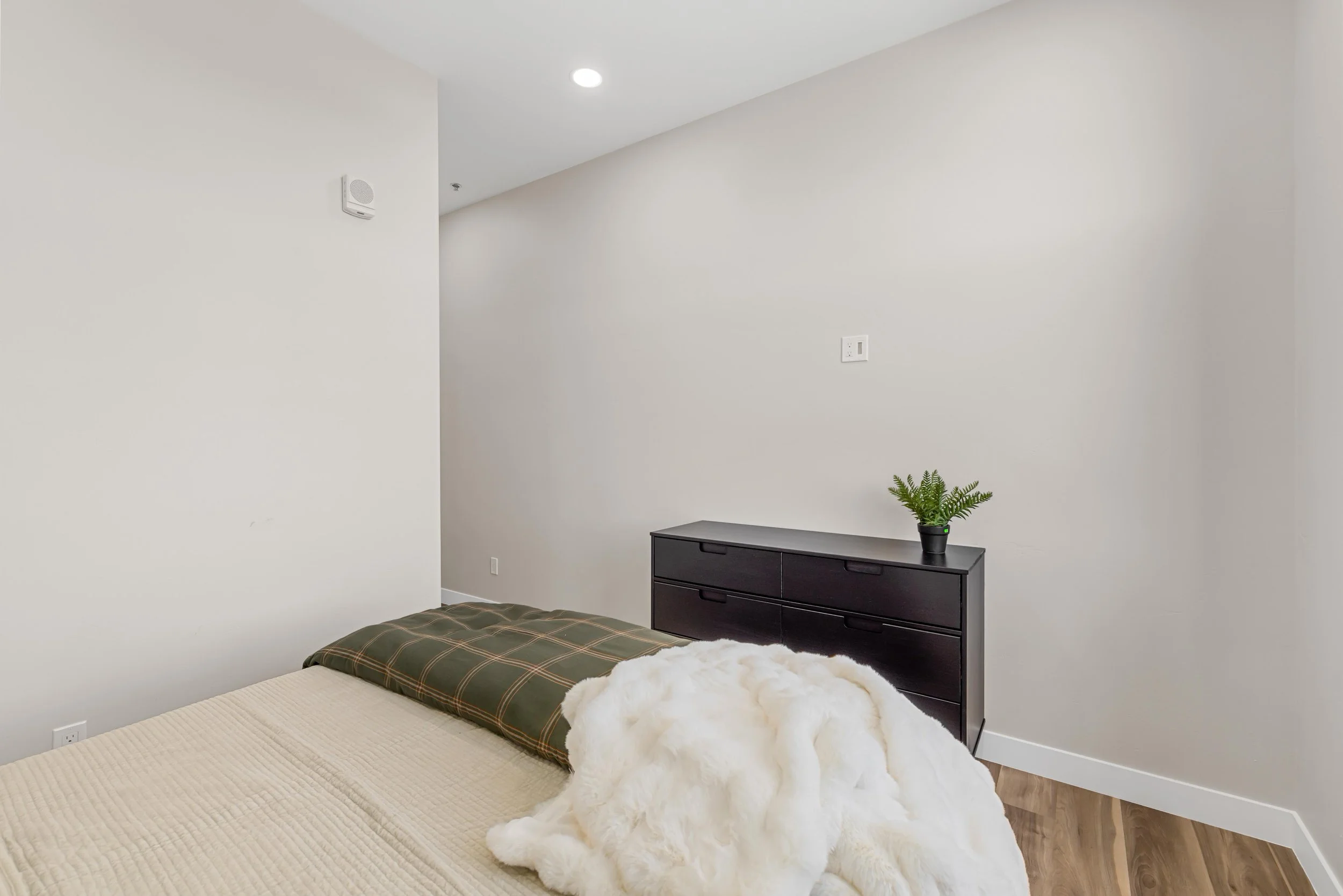 A bedroom inside an Ice Haus Condo in Sheridan, Wyoming, that is for sale. Featuring a bed, a black dresser with a potted green plant, and a small part of a beige rug. 