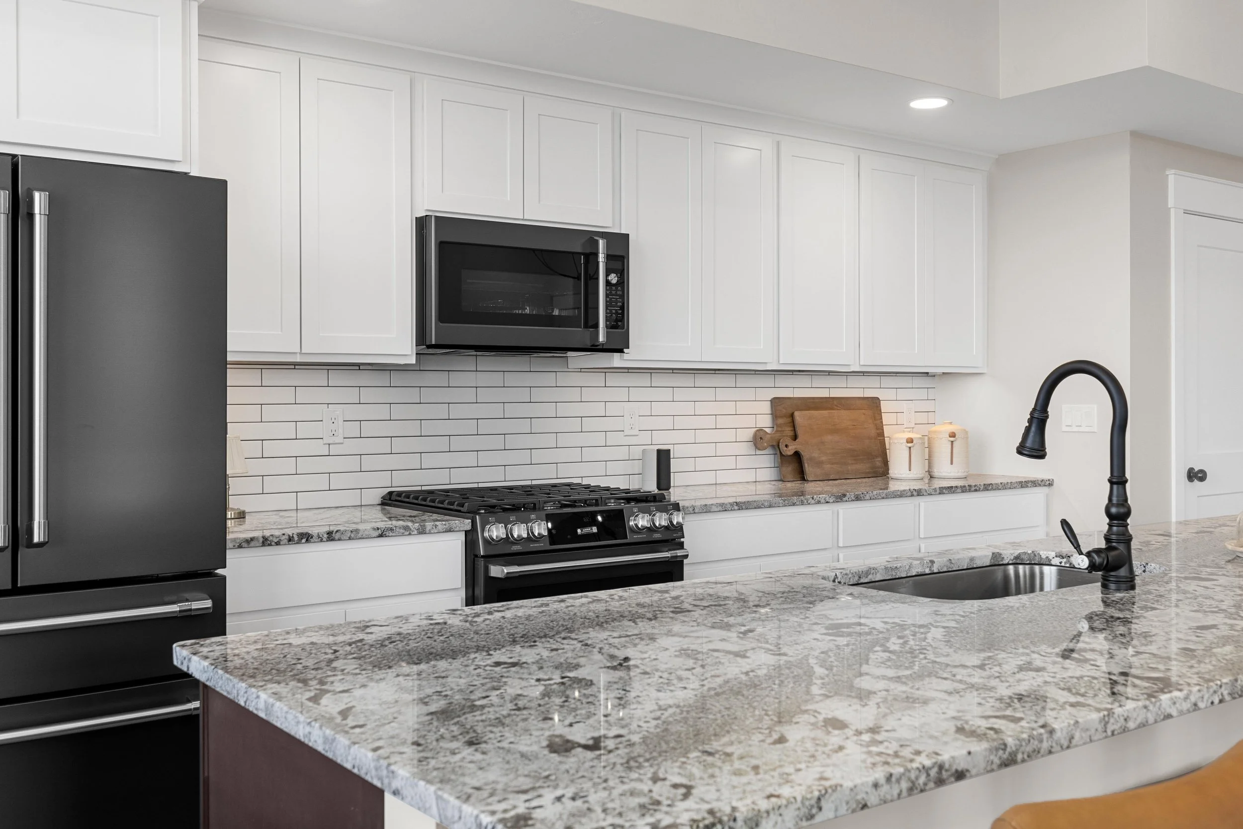 Modern kitchen with white cabinets, black appliances, granite countertop island, and a white subway tile backsplash.