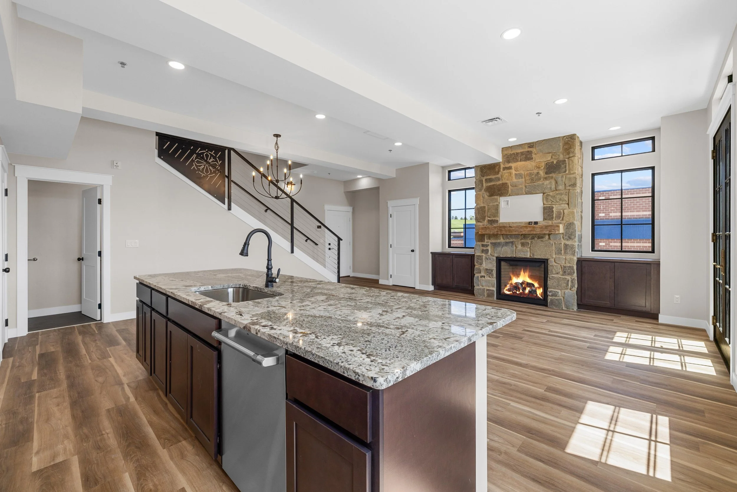 Open concept living room and kitchen with stone fireplace, large windows, and hardwood floors.