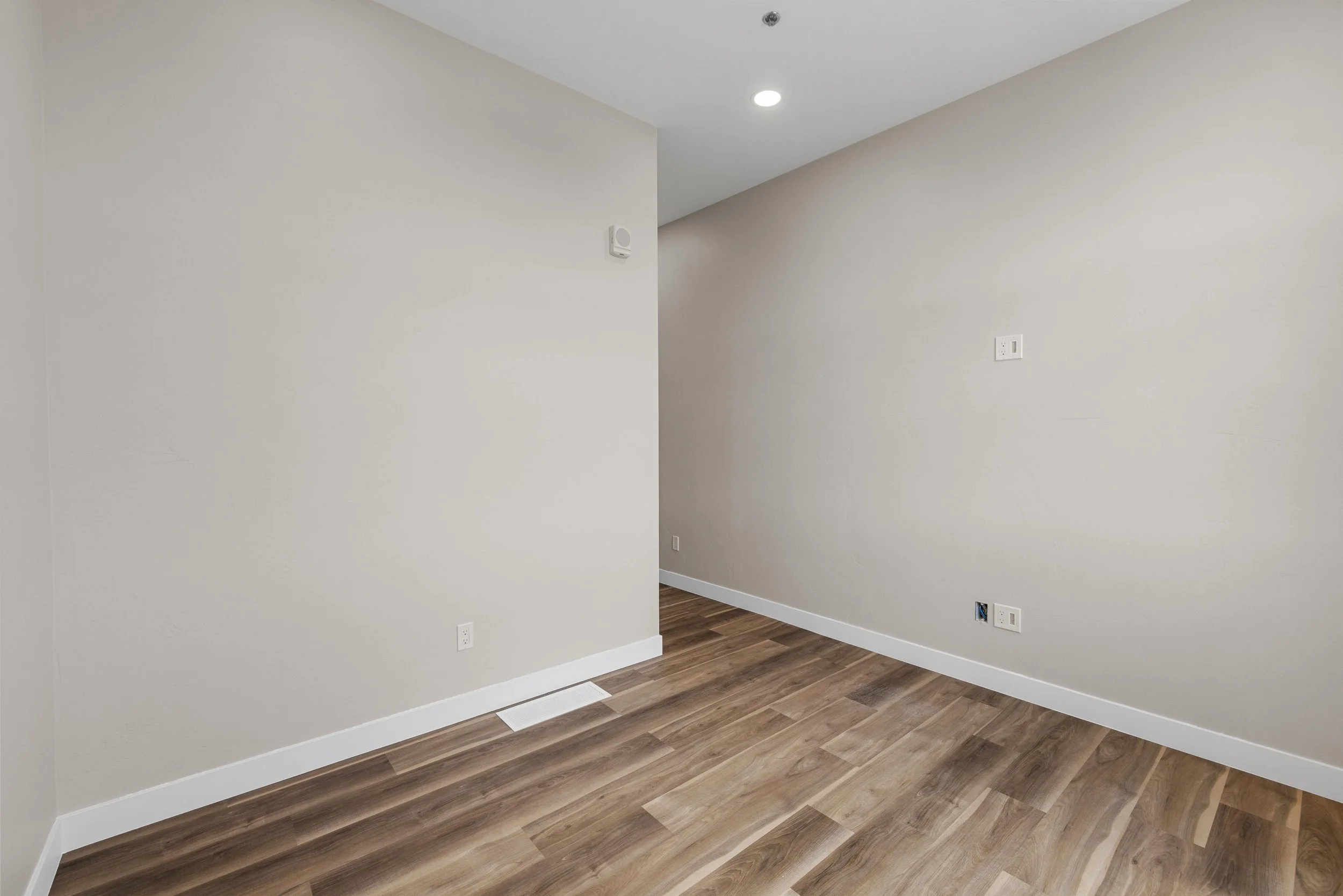 Empty room with beige walls, hardwood floor, and ceiling light fixture.
