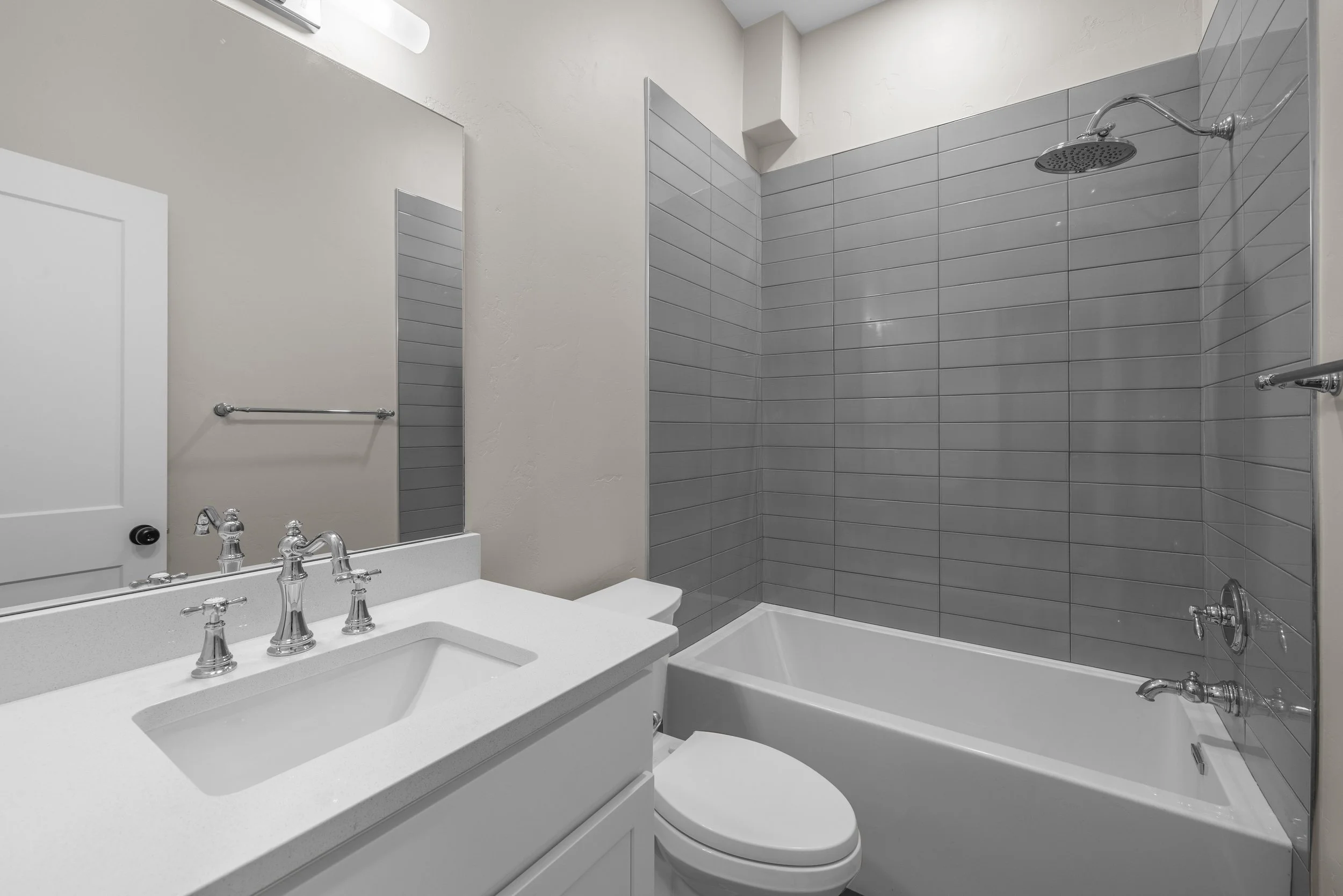 A small bathroom with a white vanity, a mirror, a toilet, and a bathtub with gray tile walls.