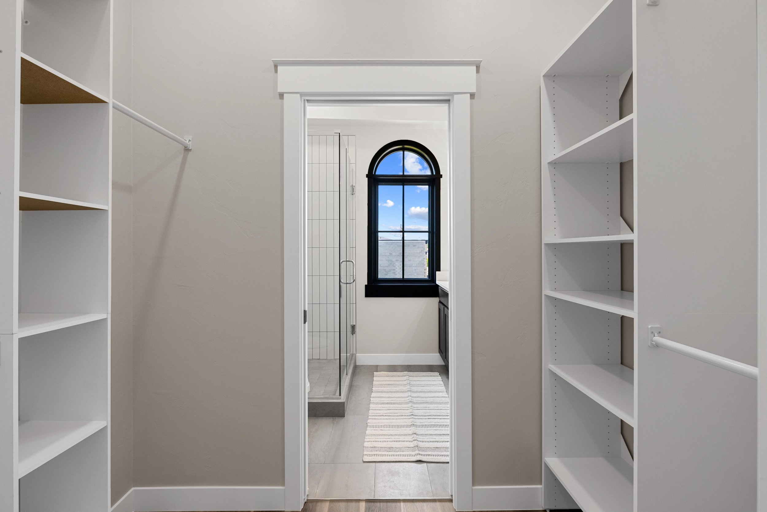 Walk-in closet and ensuite bathroom inside an Ice Haus Condo for sale in Sheridan, Wyoming, featuring built-in shelving, arched window, and modern finishes.